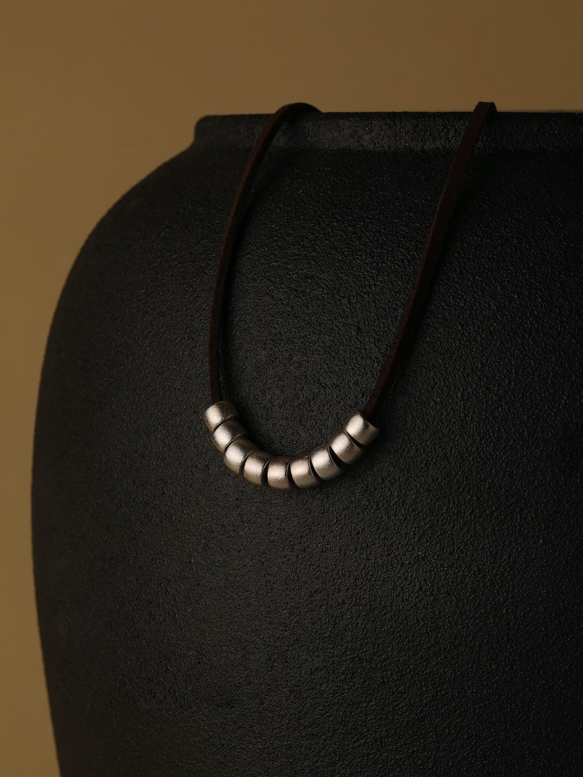 Fairyokai Balance Glide leather and silver bead necklace displayed on a dark stand against a brown background.