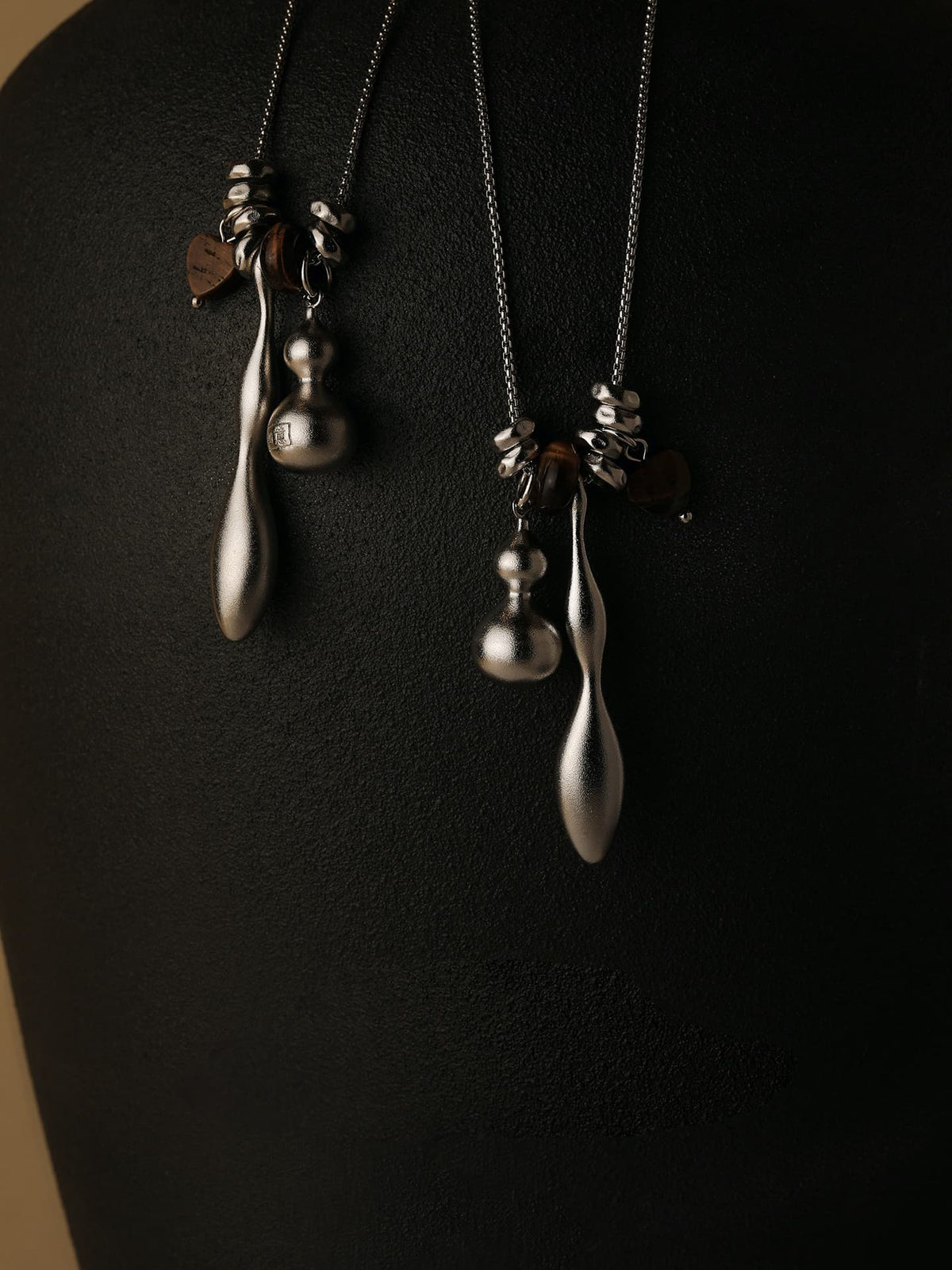 Two Fairyokai Balance Veil tiger eye gourd roller bead necklaces hanging on a dark display stand, on a dark background.