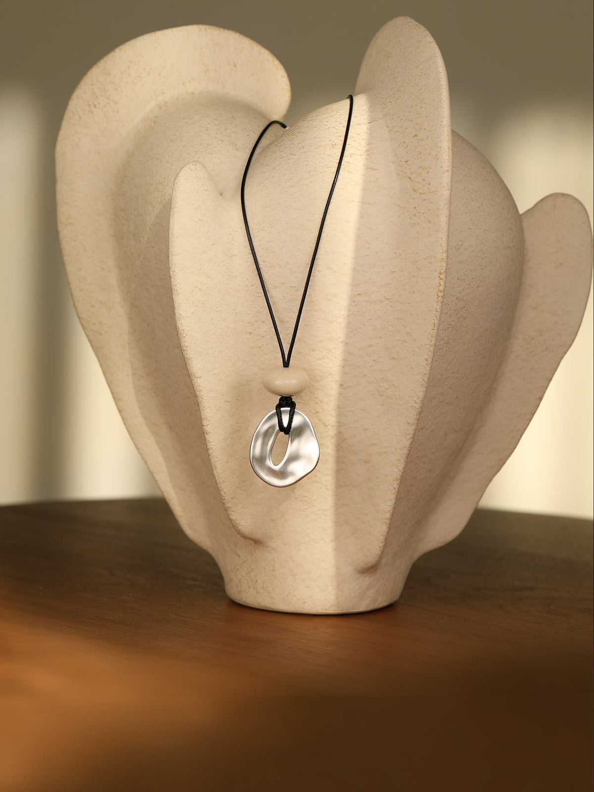 Fairyokai Breath Pendant adjustable waxed cord oval necklace hanging on a white display object placed on a brown wooden table.