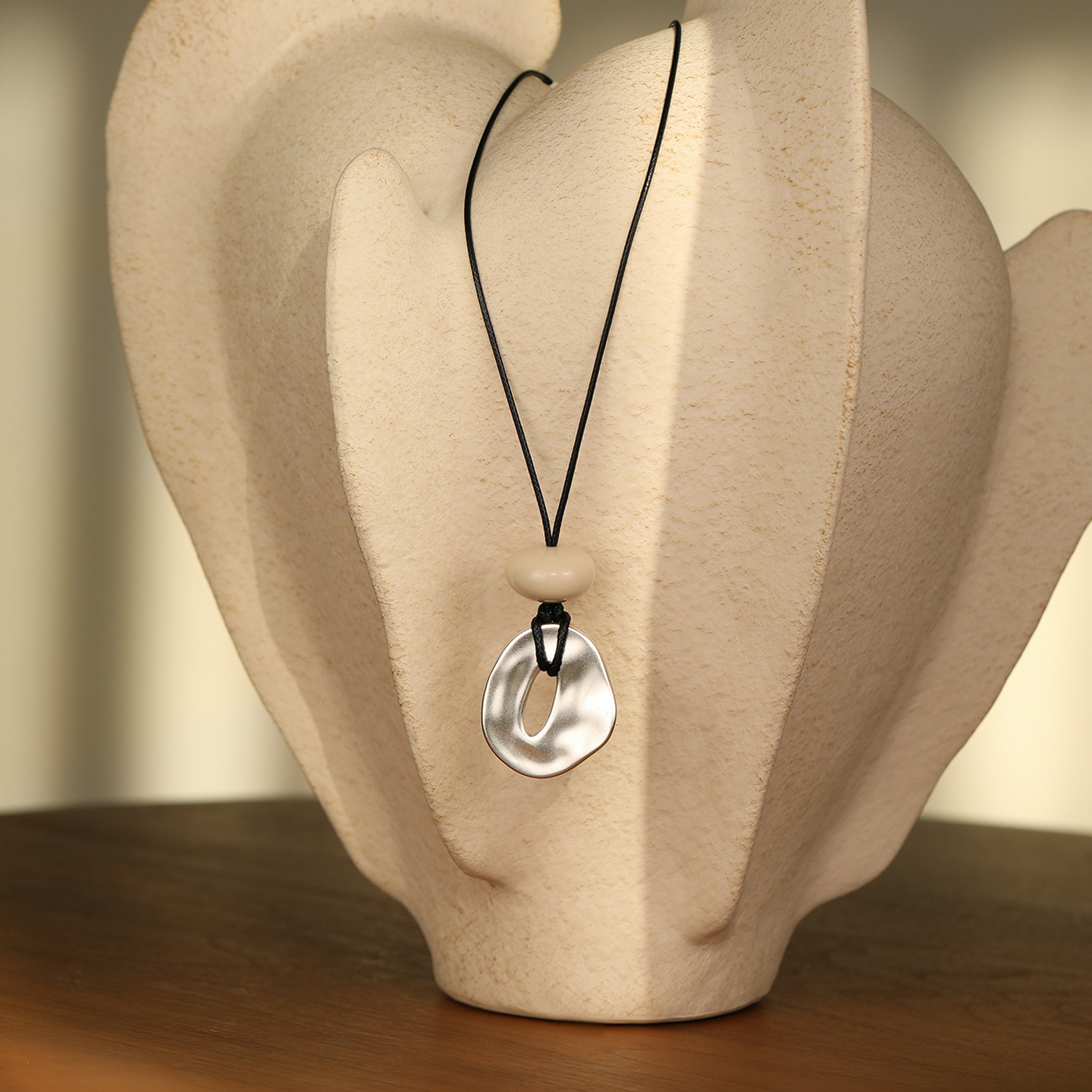 Fairyokai Breath Pendant waxed cord necklace with oval pendant, hanging on a cream-colored bottle placed on a dark brown wooden table – static close-up for homepage brand story section.