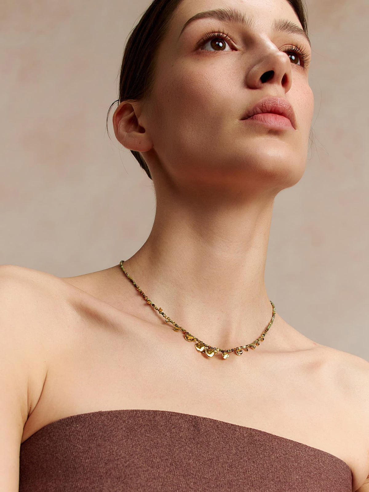 Model wearing Fairyokai Breeze Whisper gold leaf natural stone necklace, looking upward, dressed in a strapless top, on a neutral background.