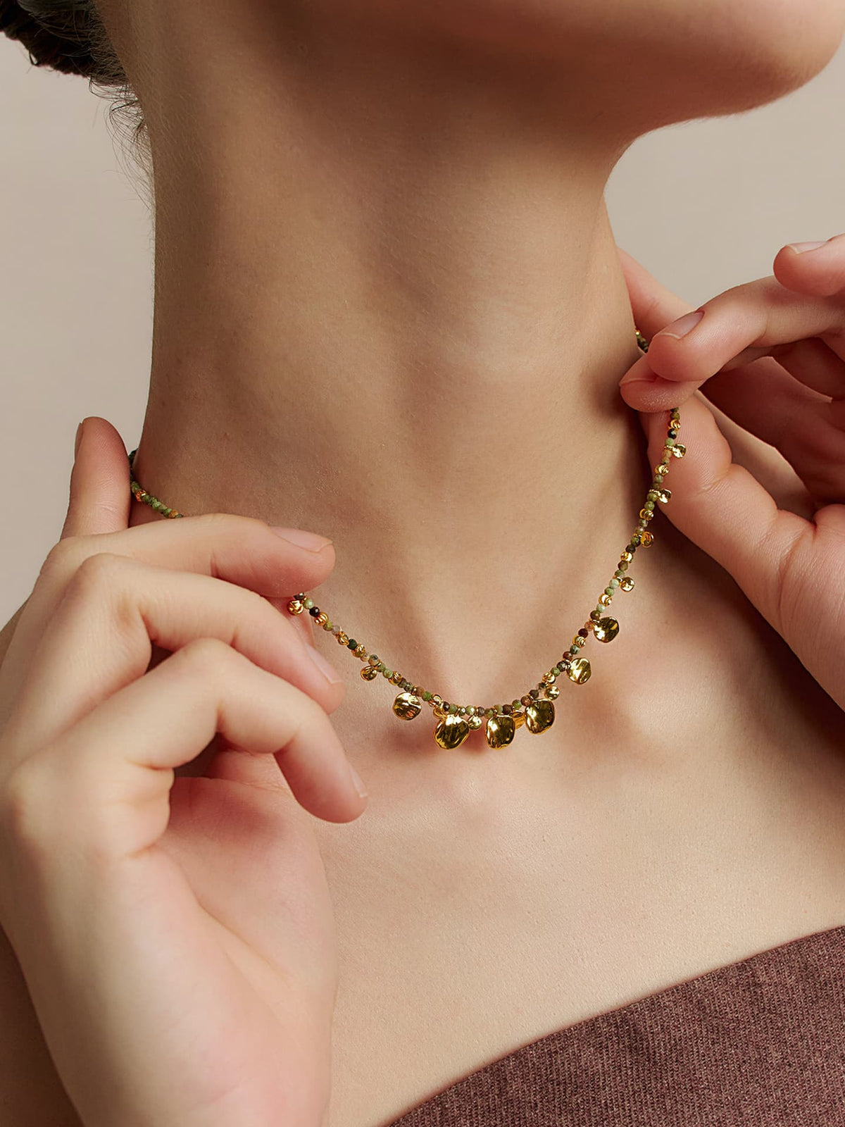 Close-up of a model wearing the Fairyokai Breeze Whisper gold leaf natural stone necklace, holding the necklace with both hands.
