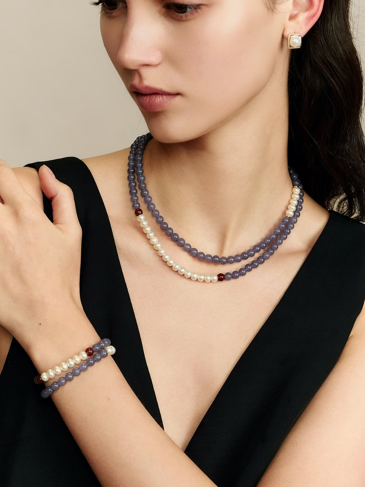 Model wearing Fairyokai Chrysoprase and Pearl double-layer necklace wrapped twice around her neck, matching bracelet on her wrist, head tilted right and looking down, in a deep V-neck black dress.