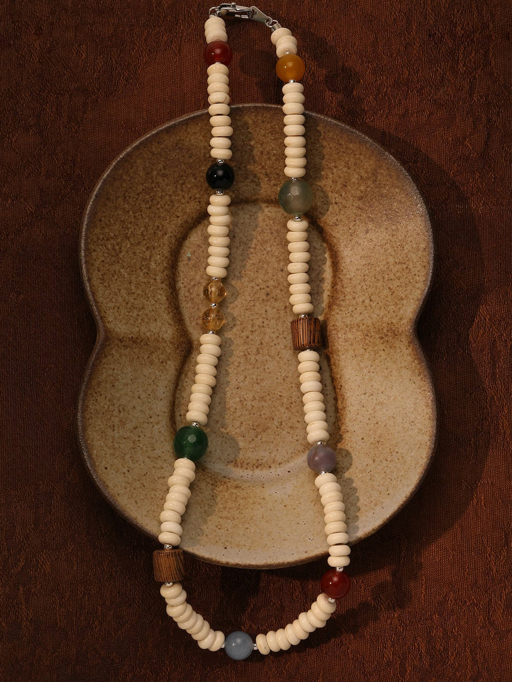 Fairyokai Color Rhythm multicolor stone roller bead necklace placed on a vintage ceramic object, top-down view (flat lay).