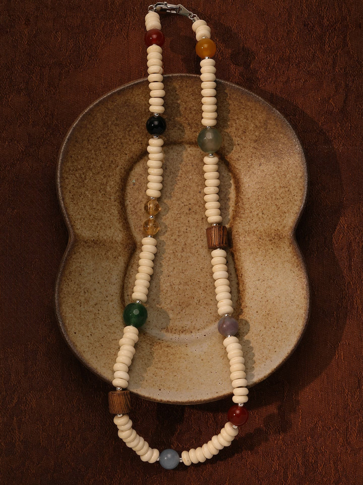 Fairyokai Color Rhythm multicolor stone roller bead necklace placed on a vintage ceramic object, top-down view (flat lay).