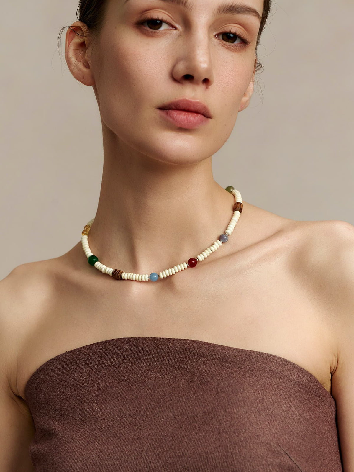Model wearing Fairyokai Color Rhythm multicolor stone roller bead necklace, facing the camera, dressed in a strapless top, on a neutral background.