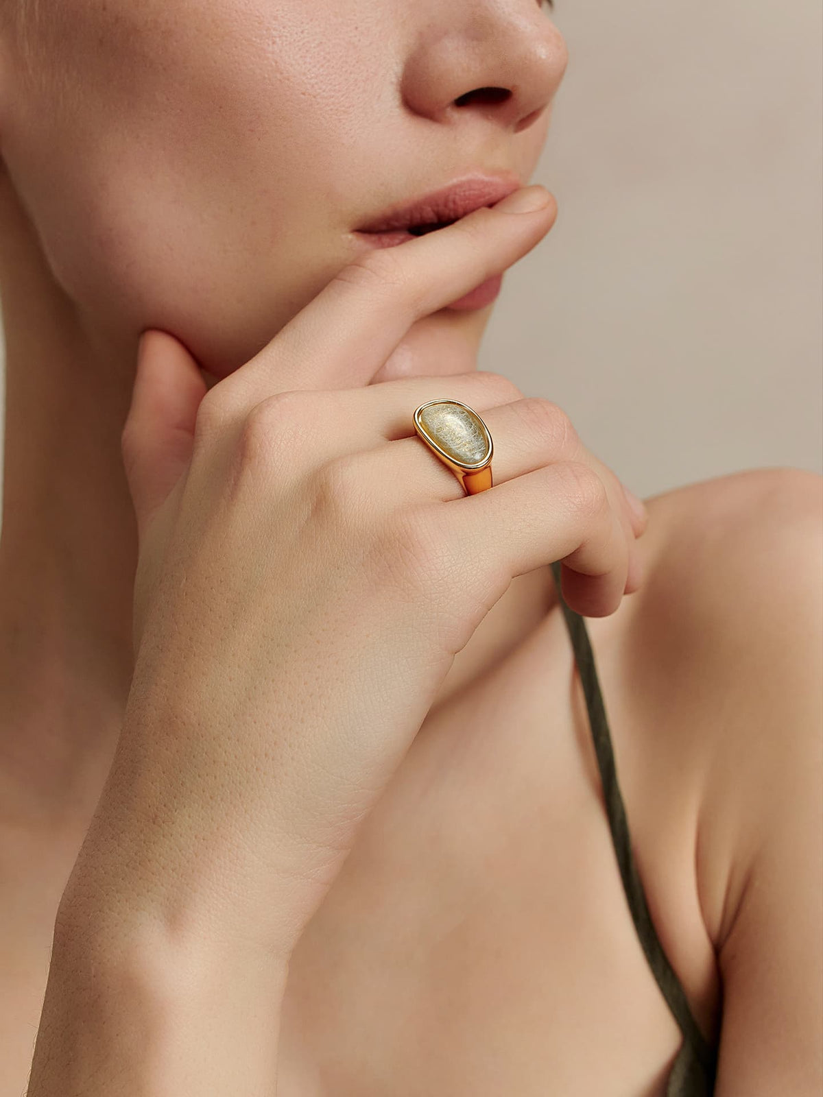 Close-up of a model wearing the Fairyokai Crack Light resin gold ring, hand resting near the chin on a beige background.