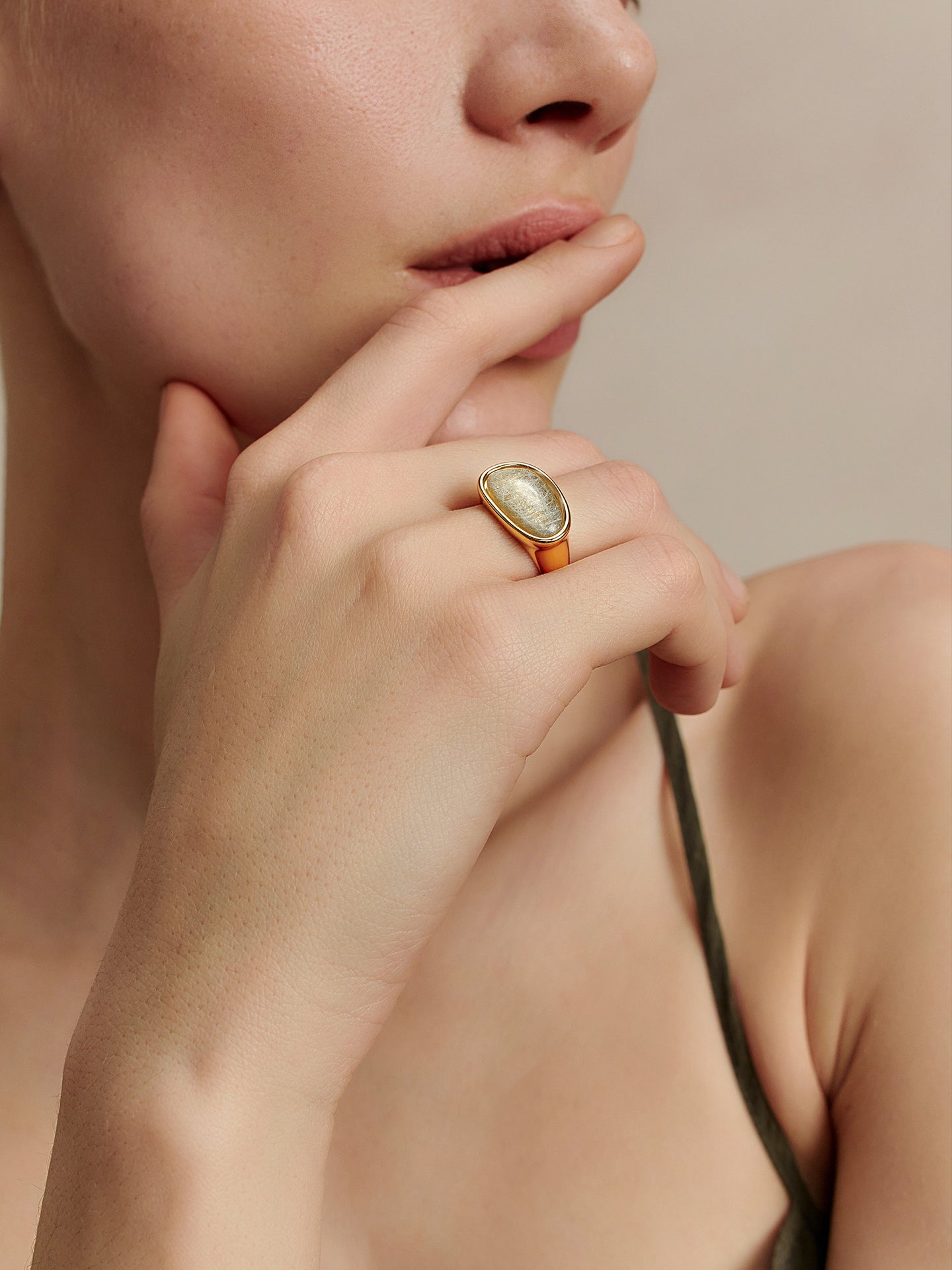 Close-up of a model wearing the Fairyokai Crack Light resin gold ring, hand resting near the chin on a beige background.