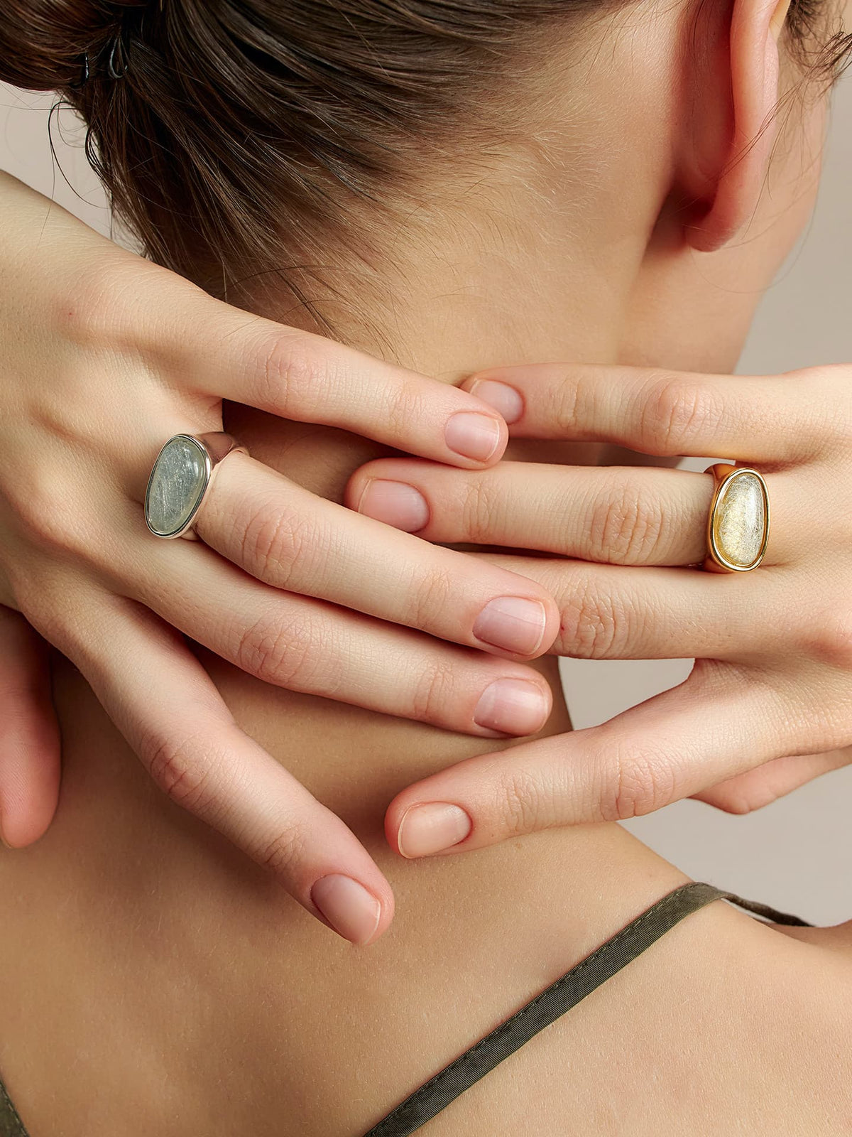 Close-up of a model wearing two Fairyokai Crack Light resin rings, hands resting behind the neck with gold and silver tones visible.