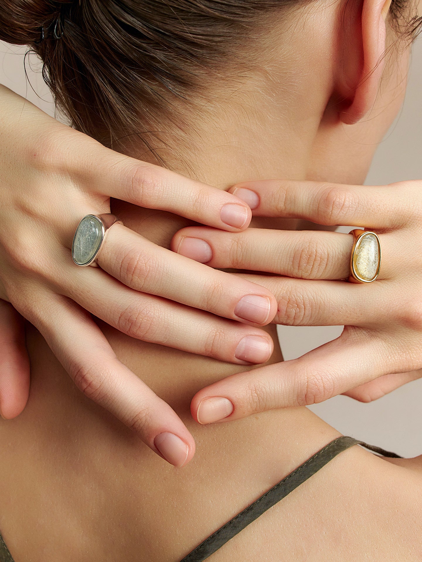 Close-up of a model wearing two Fairyokai Crack Light resin rings, hands resting behind the neck with gold and silver tones visible.