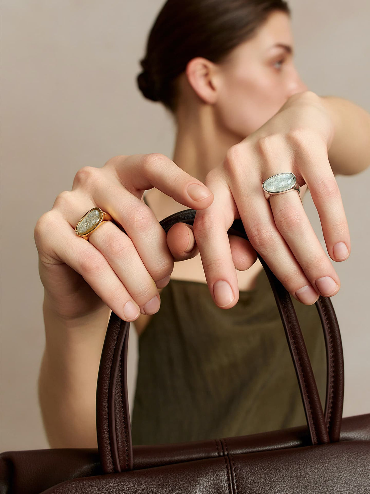 Model holding a brown leather bag while wearing the Fairyokai Crack Light resin gold ring, with the ring visible on the hand.