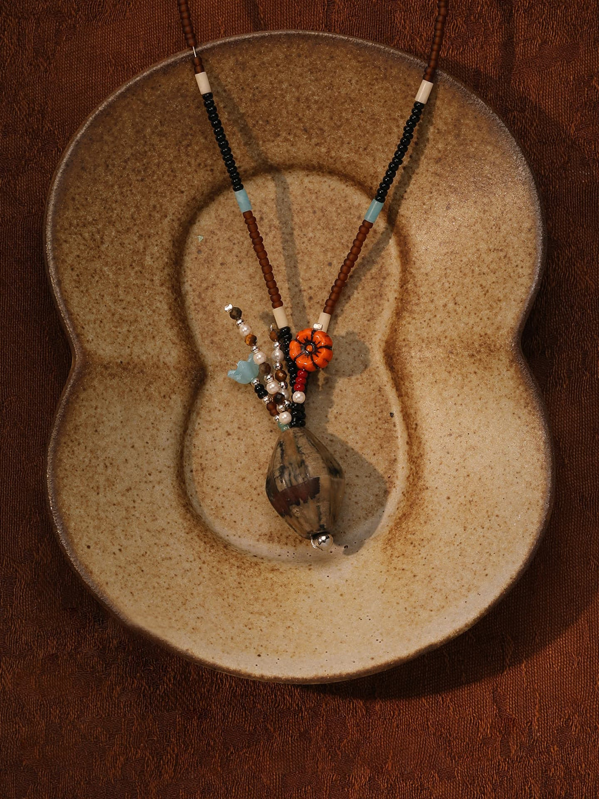 Fairyokai Culling the Cream agate vase pendant necklace placed on a vintage ceramic object, top-down view (flat lay).