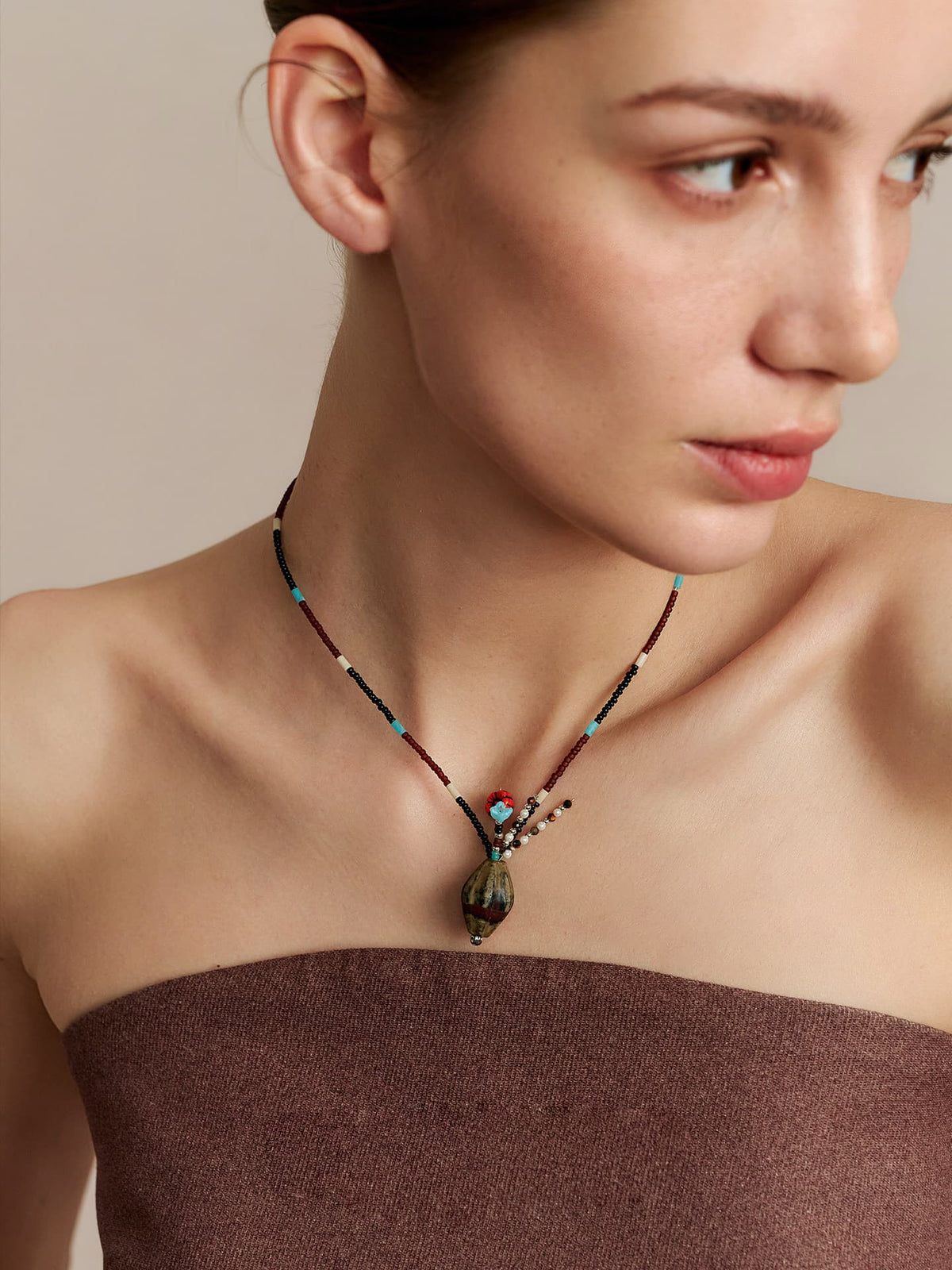 Model in a strapless top, looking to the left, wearing the Fairyokai Culling the Cream agate vase pendant necklace, close-up from chest up.