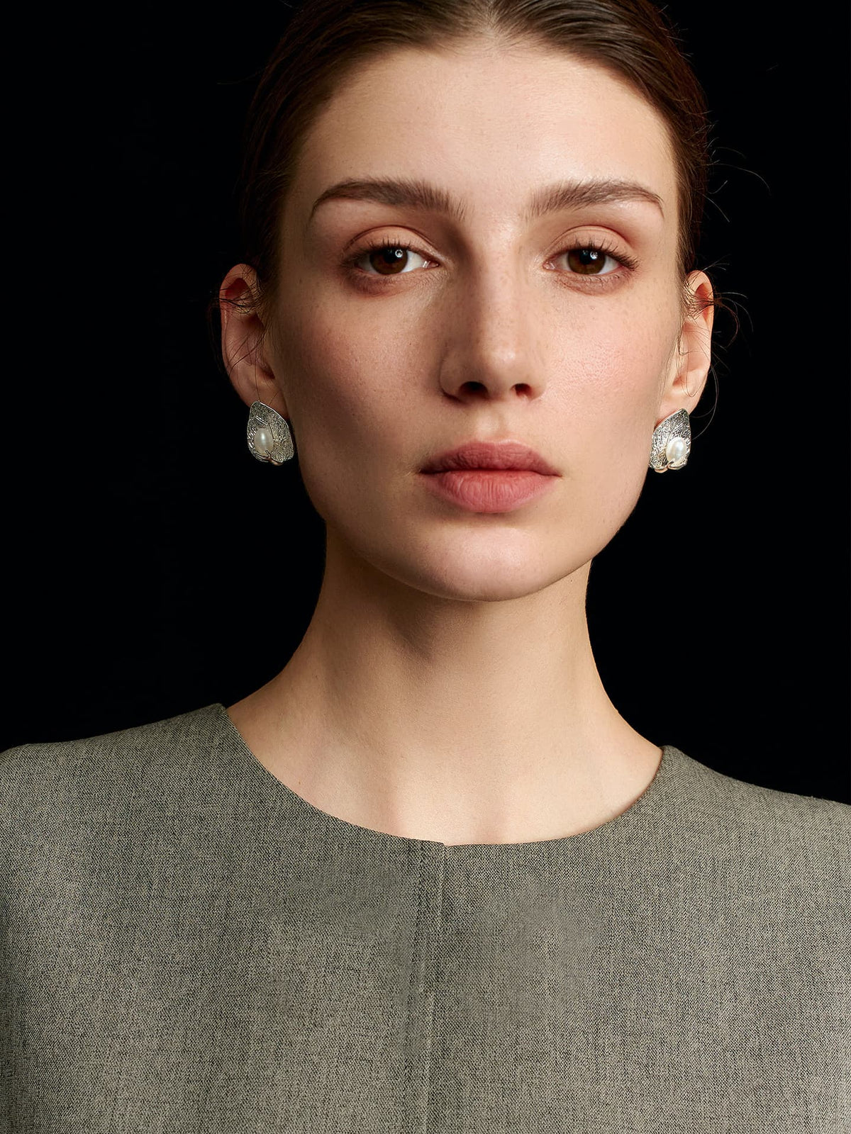 Model in a solid sleeveless top wearing Fairyokai Dew-Catching leaf and palm earrings, facing the camera on a black background.