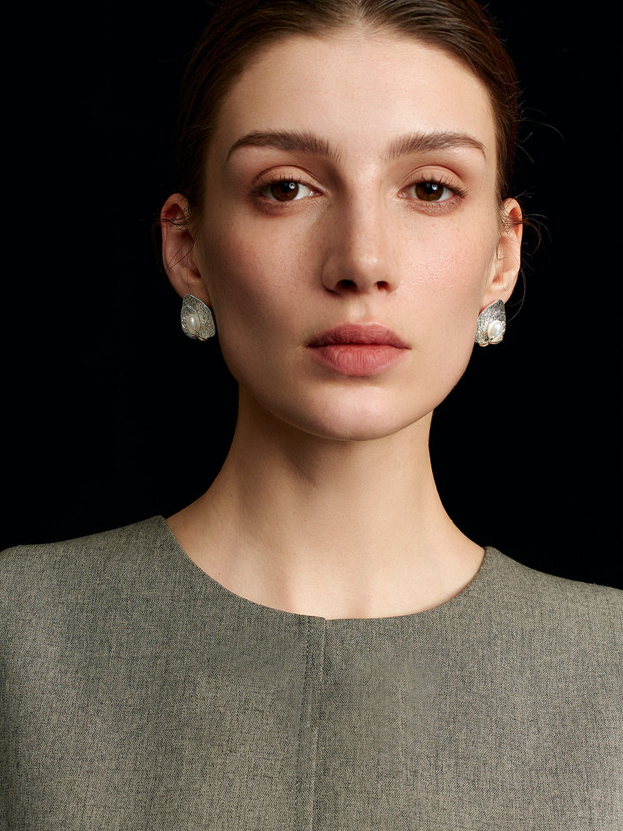 Model in a solid sleeveless top wearing Fairyokai Dew-Catching leaf and palm earrings, facing the camera on a black background.