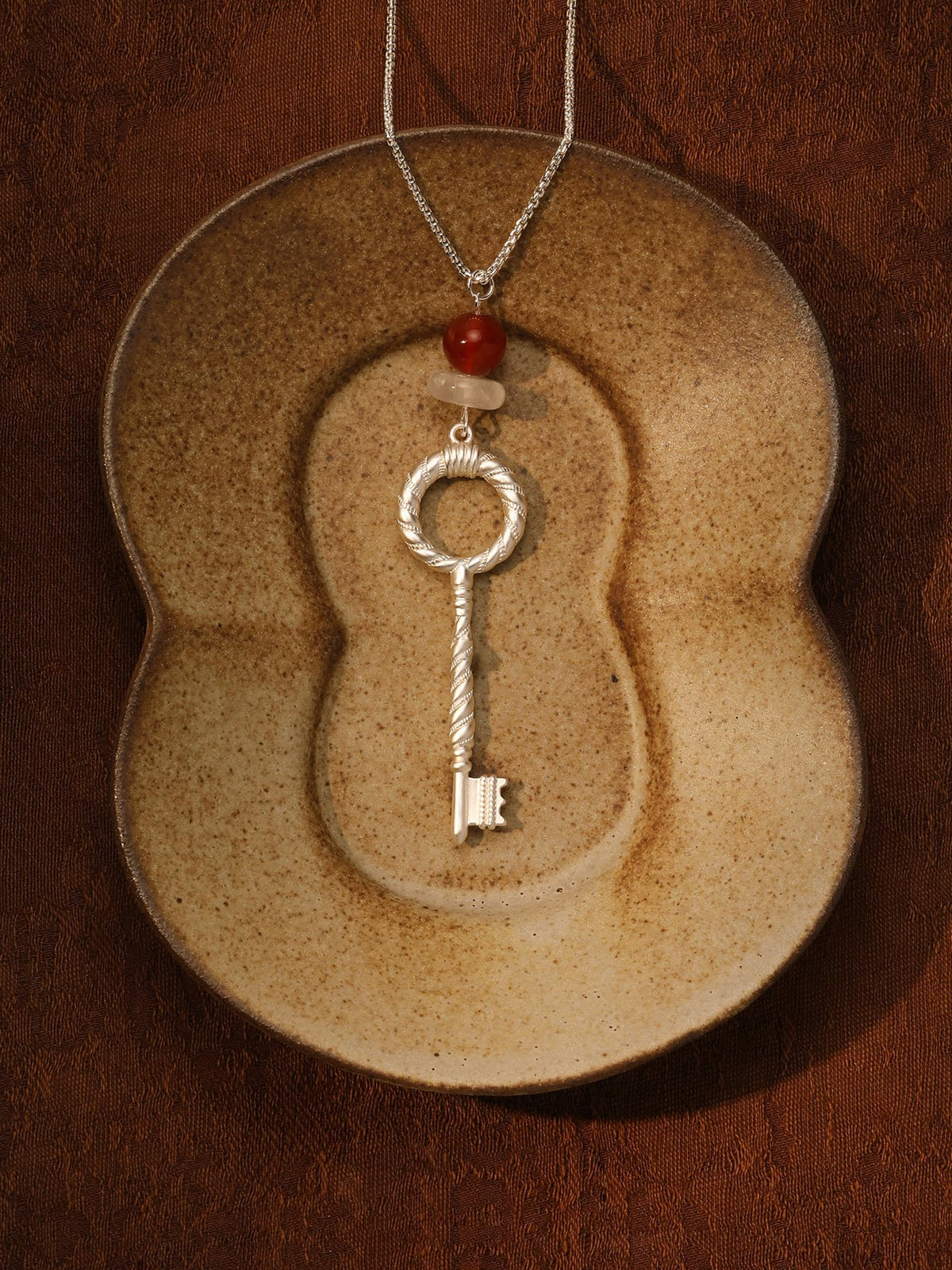Fairyokai Dream Key red agate crystal key pendant necklace placed on a vintage ceramic object, top-down view (flat lay).