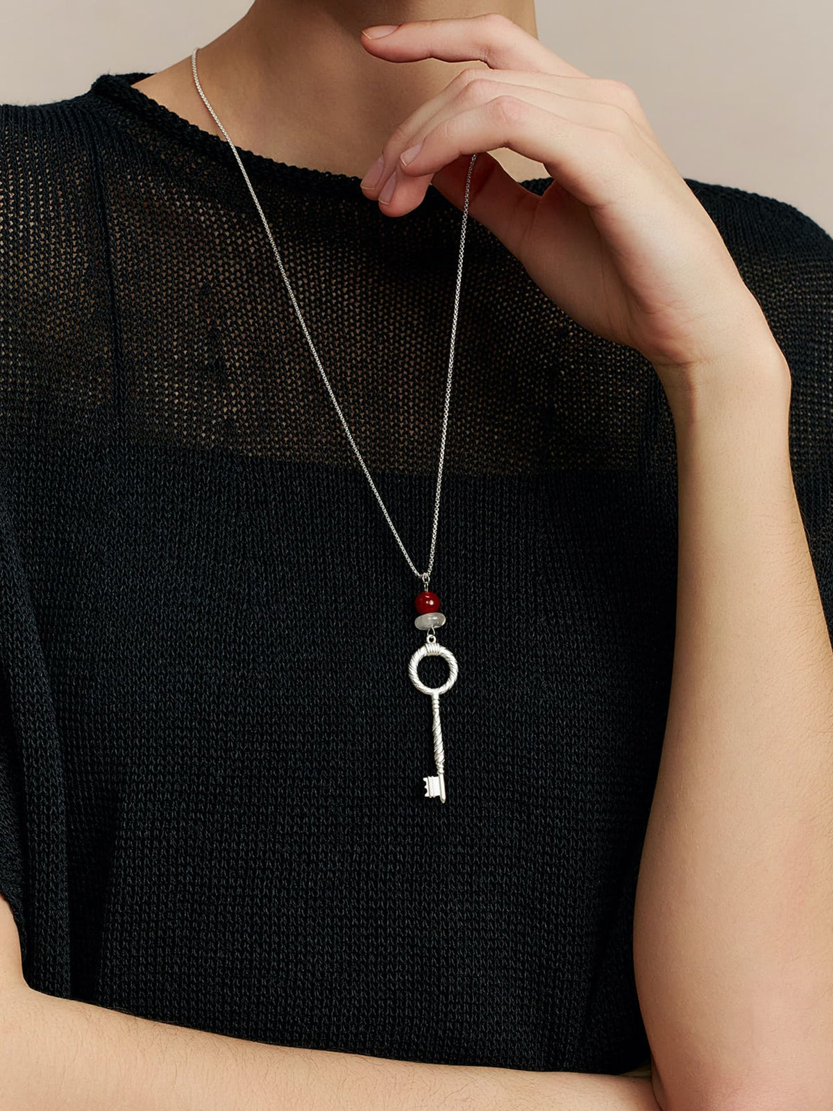 Model in a black top, one hand resting on her chin, facing forward, wearing the Fairyokai Dream Key red agate crystal key pendant necklace. Close-up from below the head focusing on the necklace hanging at her chest.
