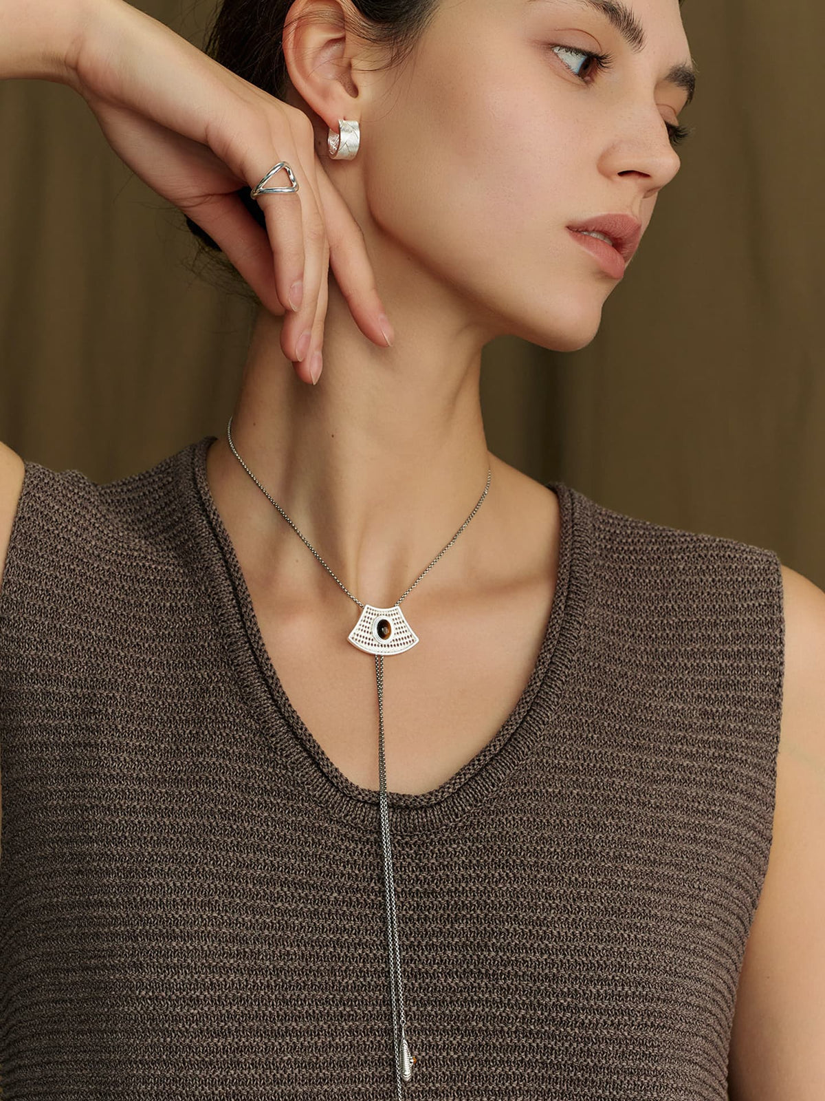 Model in a sleeveless knit top, wearing the Fairyokai Flowing River adjustable tiger eye fan necklace, looking down to the left, with her right hand raised touching her right ear.