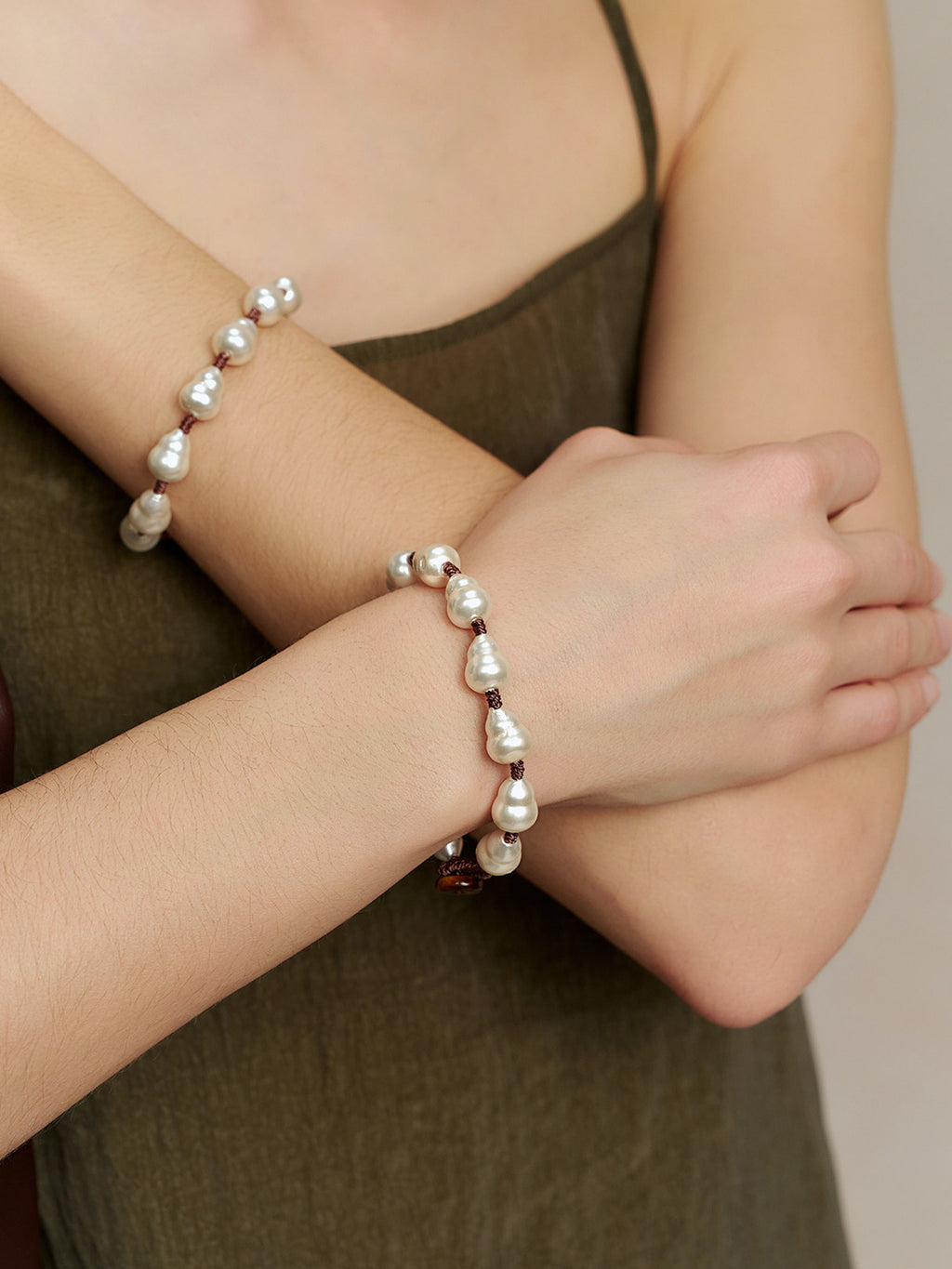Close-up of a model wearing the Fairyokai Full Embrace faux pearl bracelet on the wrist, with pearl beads visible against an olive dress.