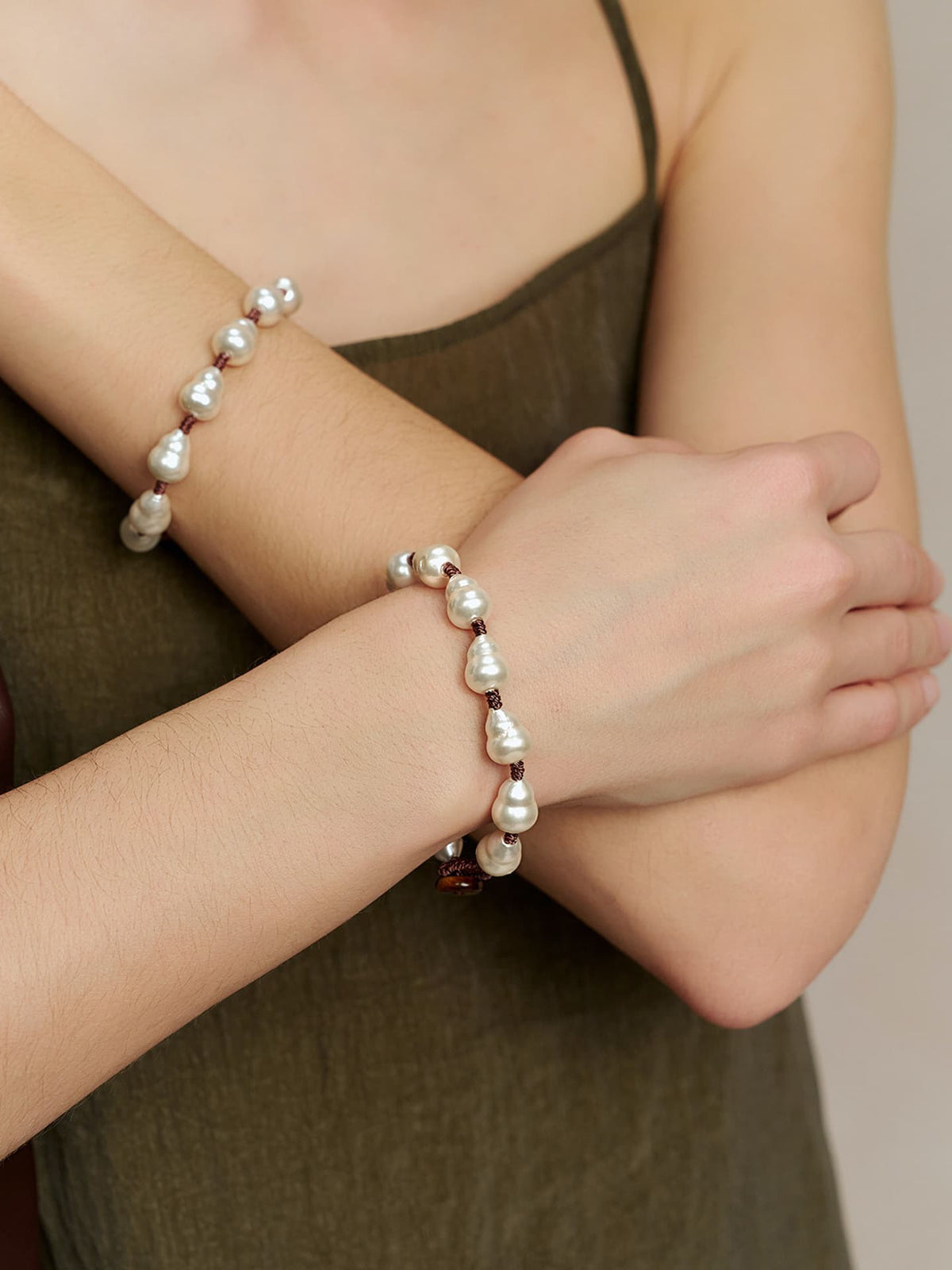 Close-up of a model wearing the Fairyokai Full Embrace faux pearl bracelet on the wrist, with pearl beads visible against an olive dress.