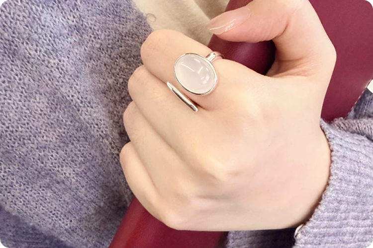 Close-up of a hand wearing a Fairyokai Open Chord Silver Natural Stone Ring, holding a red notebook.