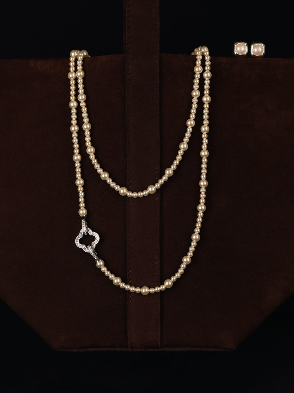 Fairyokai Layered Abundance alternating faux pearl necklace draped over a dark brown bag against a black background.