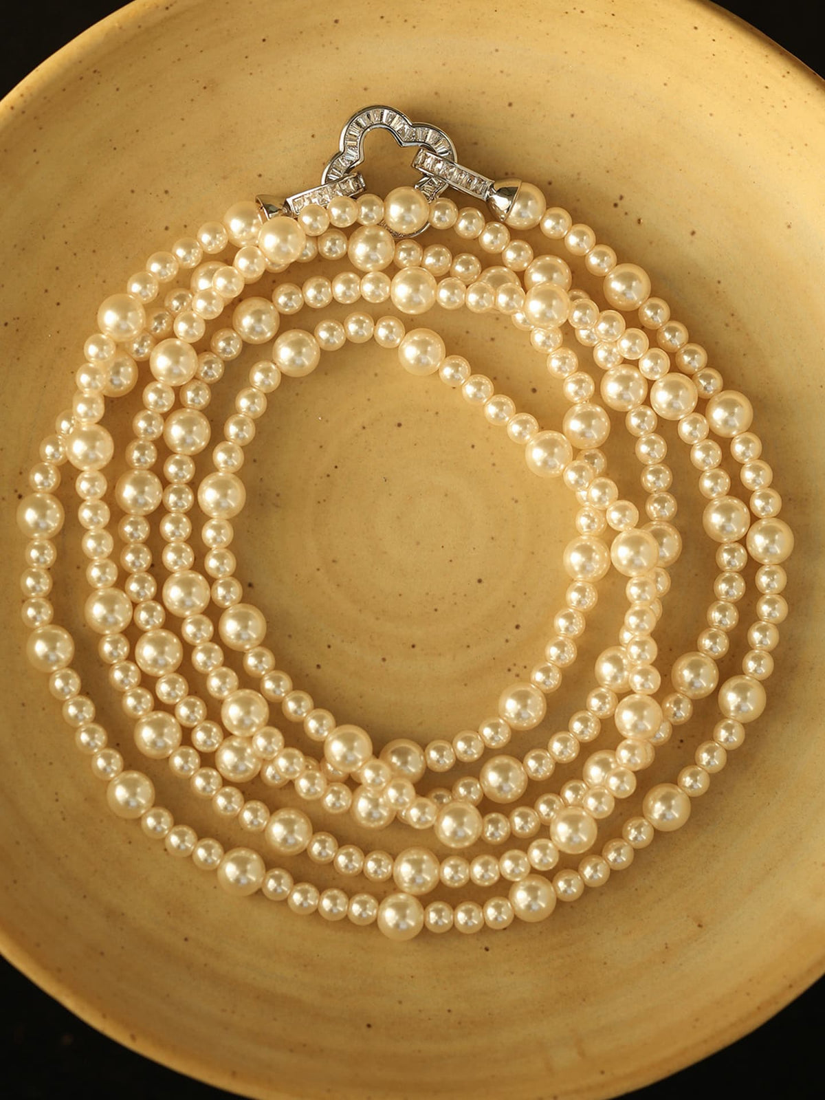 Fairyokai Layered Abundance alternating faux pearl necklace arranged on a round plate, top-down view.