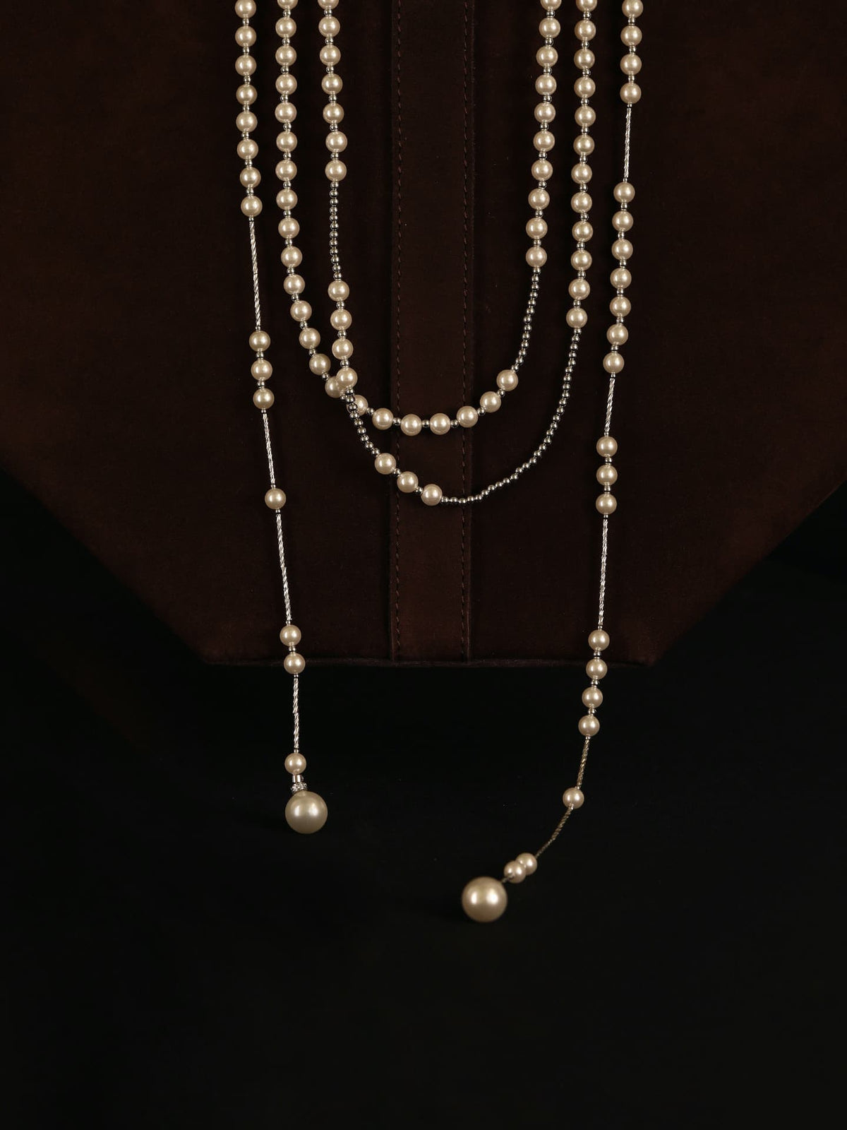 Fairyokai Layered Breath adjustable double-layer faux pearl necklace hanging over a dark brown bag on a black background.