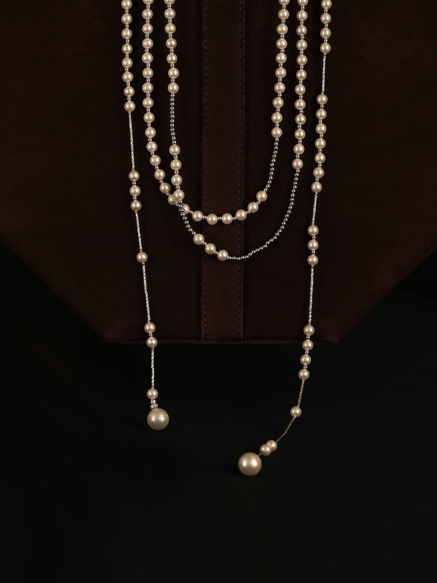 Fairyokai Layered Breath adjustable double-layer faux pearl necklace hanging over a dark brown bag on a black background.