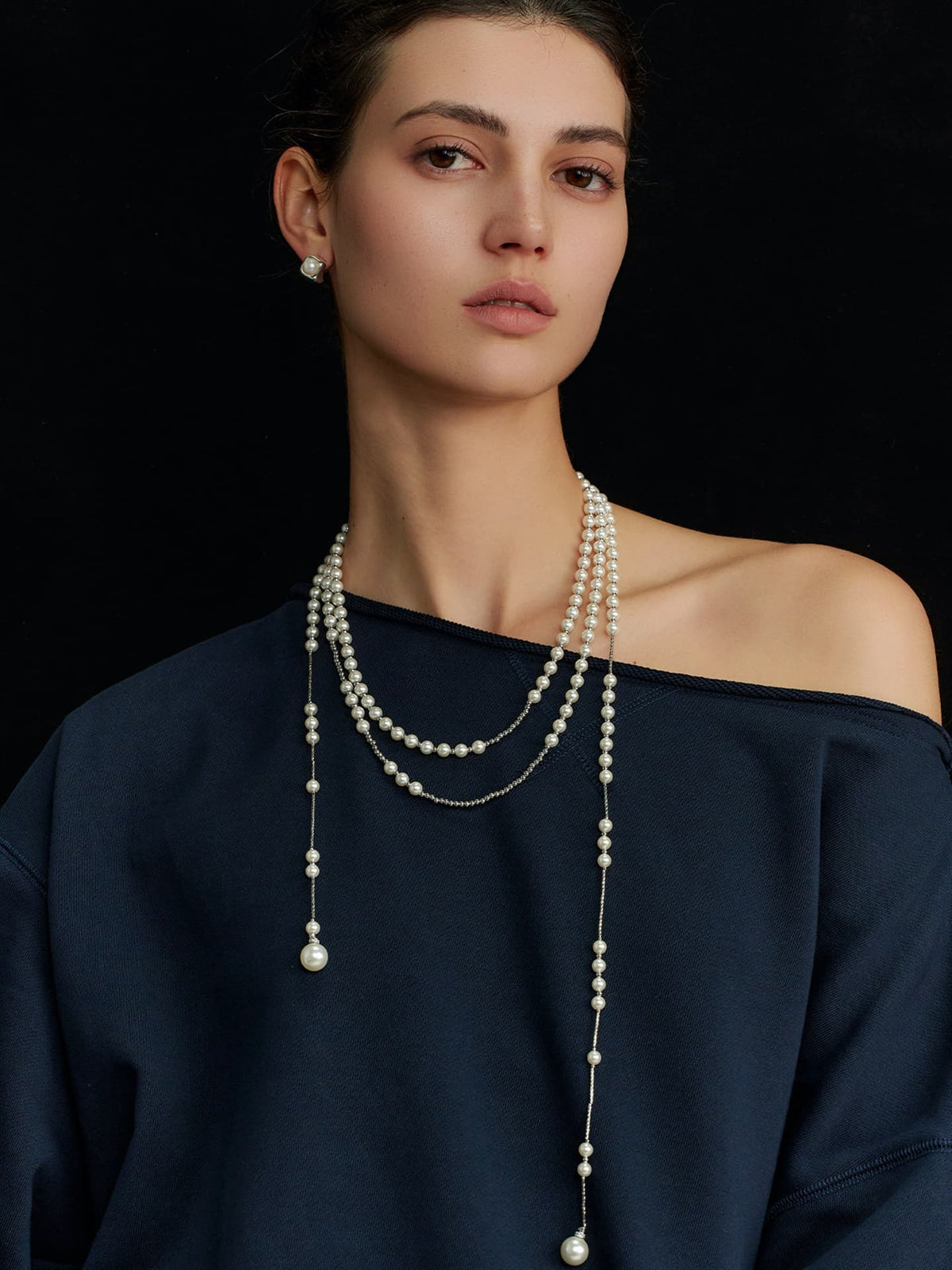 Model in a navy top wearing the Fairyokai Layered Breath adjustable double-layer faux pearl necklace, facing the camera on a black background.
