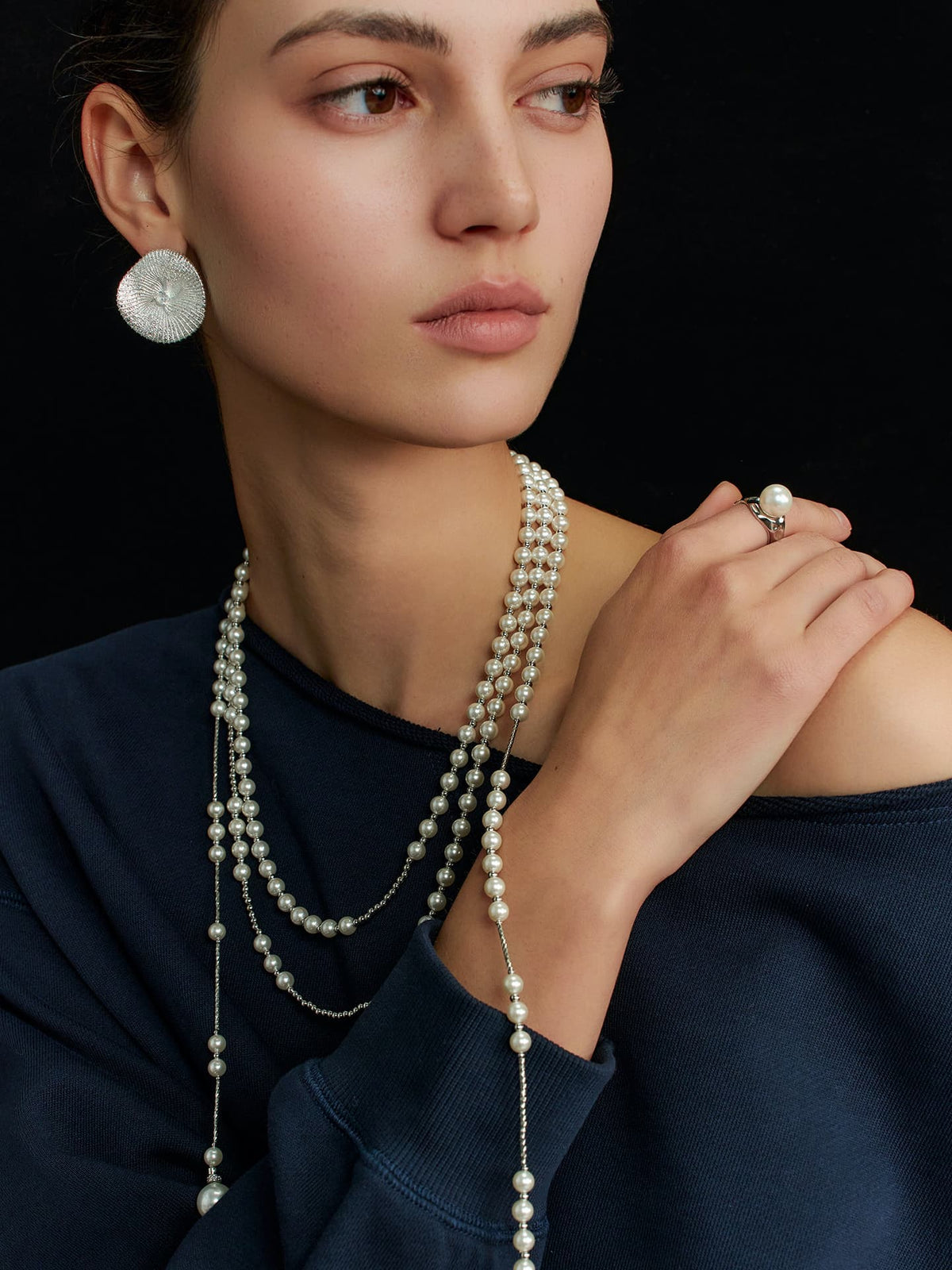 Model in a navy top, looking to the left against a black background, with her right hand resting on her left exposed shoulder, wearing the Fairyokai Layered Breath adjustable double-layer faux pearl necklace.