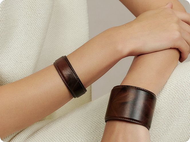 Close up of a woman wearing Fairyokai vein cuff PU leather set bracelet, with her arms on her leg, on a white background.