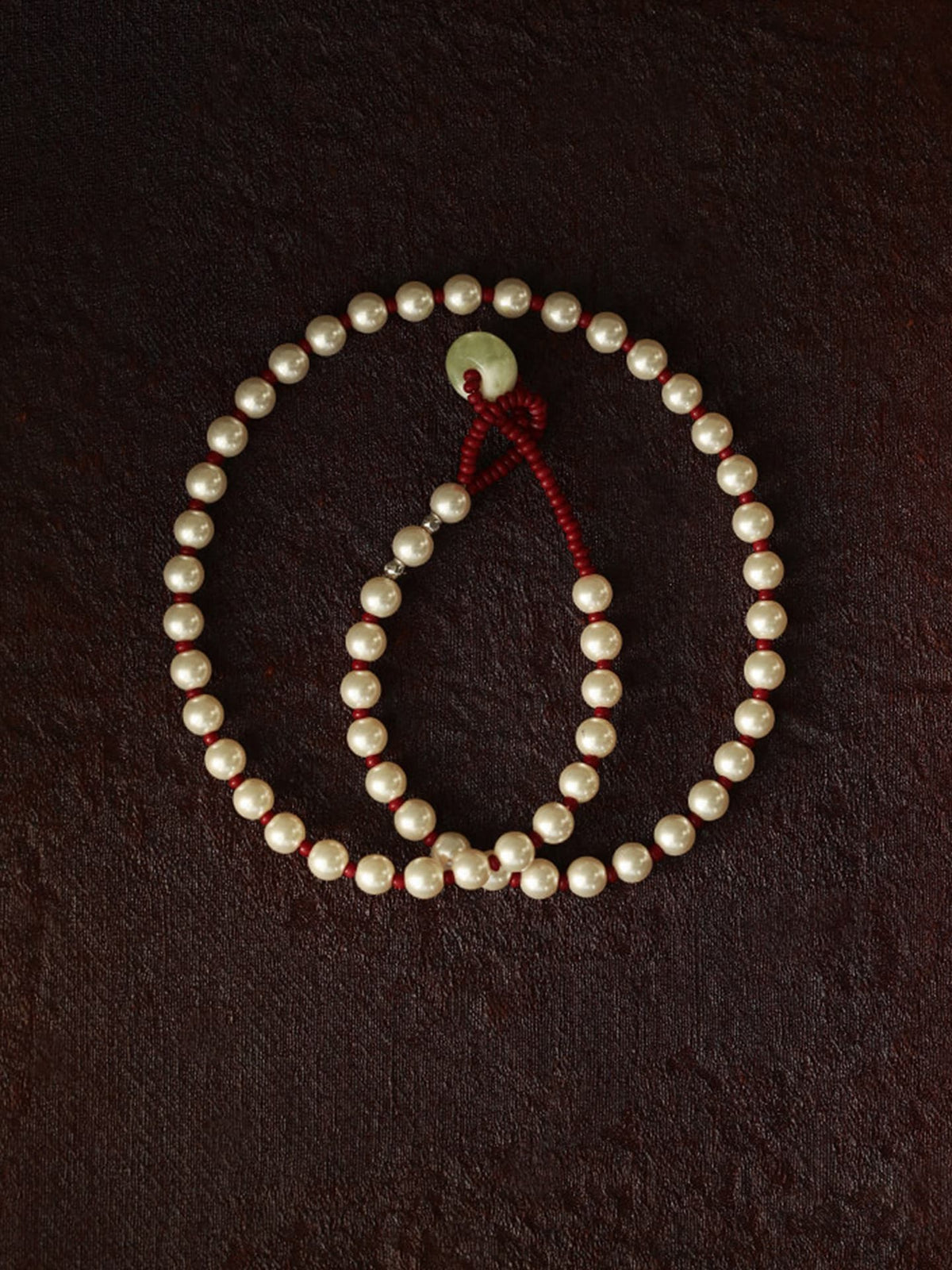Fairyokai Lunar Chord Czech bead and jade pearl necklace (red) on a dark brown background.