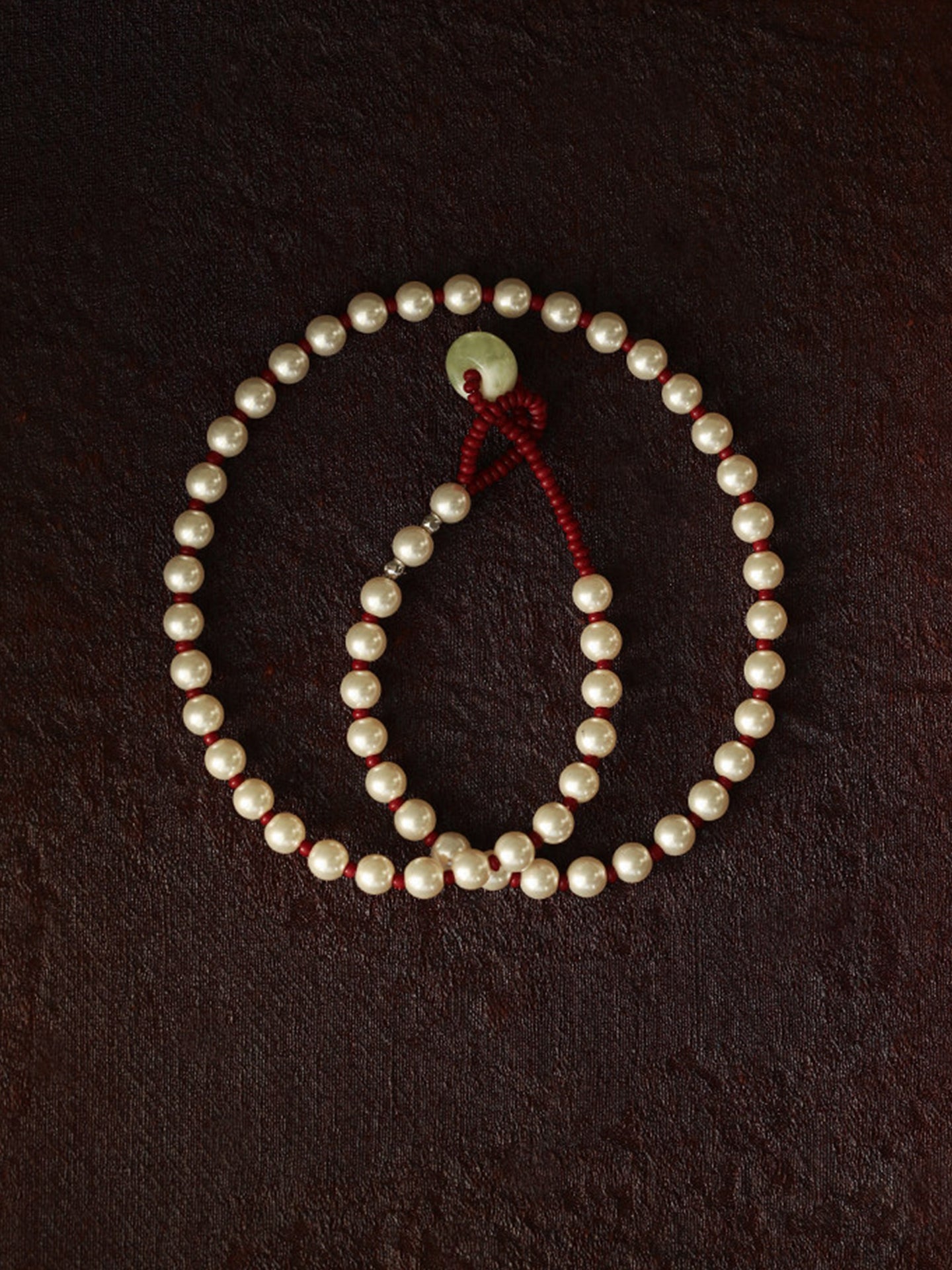 Fairyokai Lunar Chord Czech bead and jade pearl necklace (red) on a dark brown background.