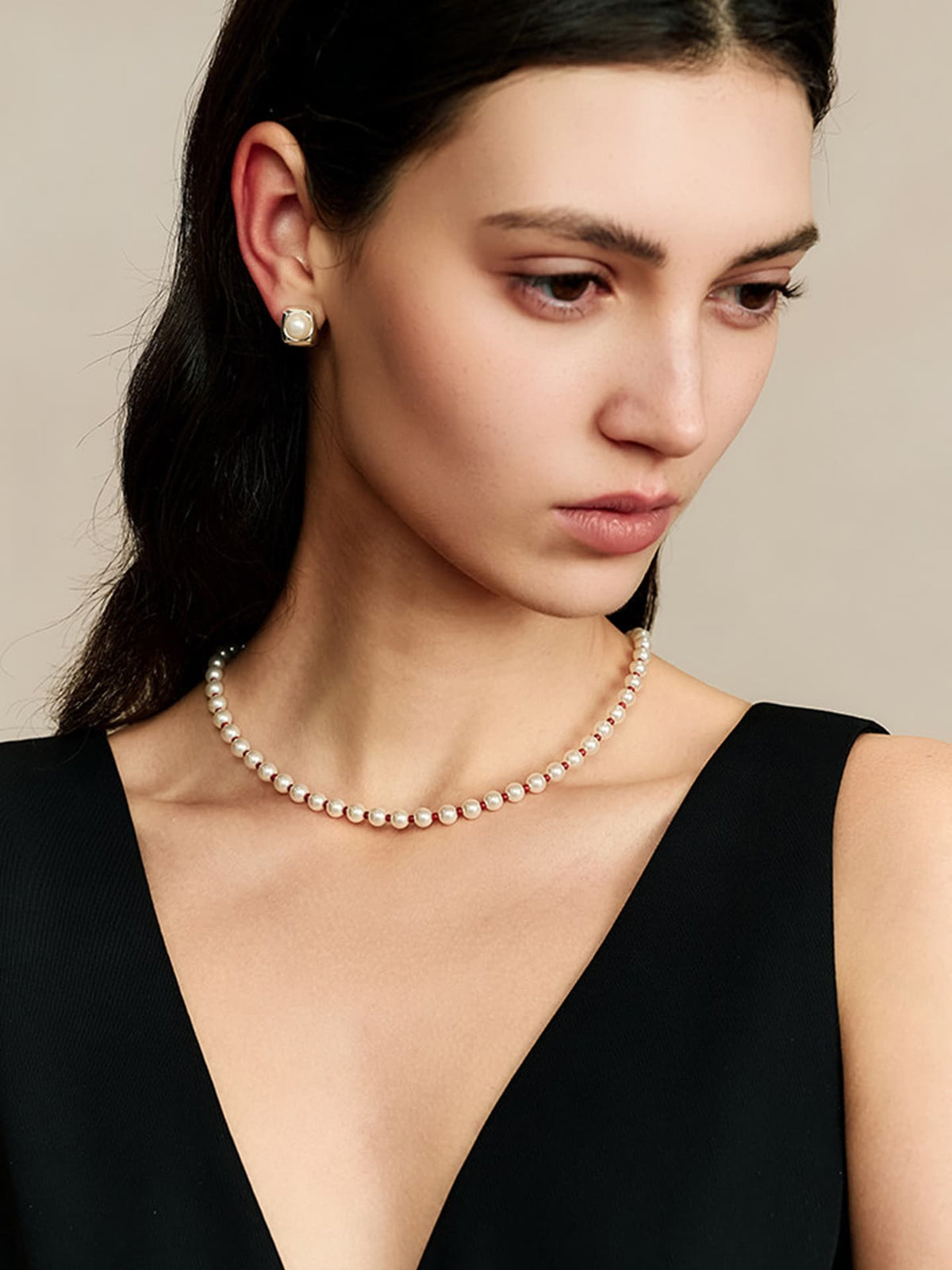 Model in a black V-neck sleeveless top wearing the Fairyokai Lunar Chord red Czech bead and jade pearl necklace, looking down to the left, close-up from chest up.