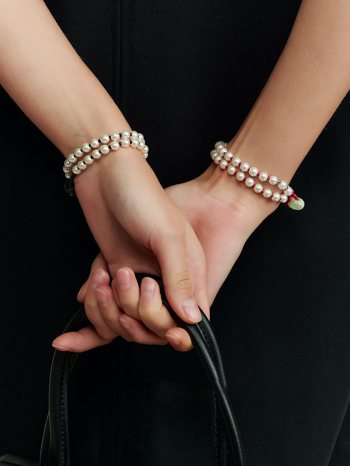 Model holding a black bag while wearing the Fairyokai Lunar Chord double-layer faux pearl bracelet on both wrists.