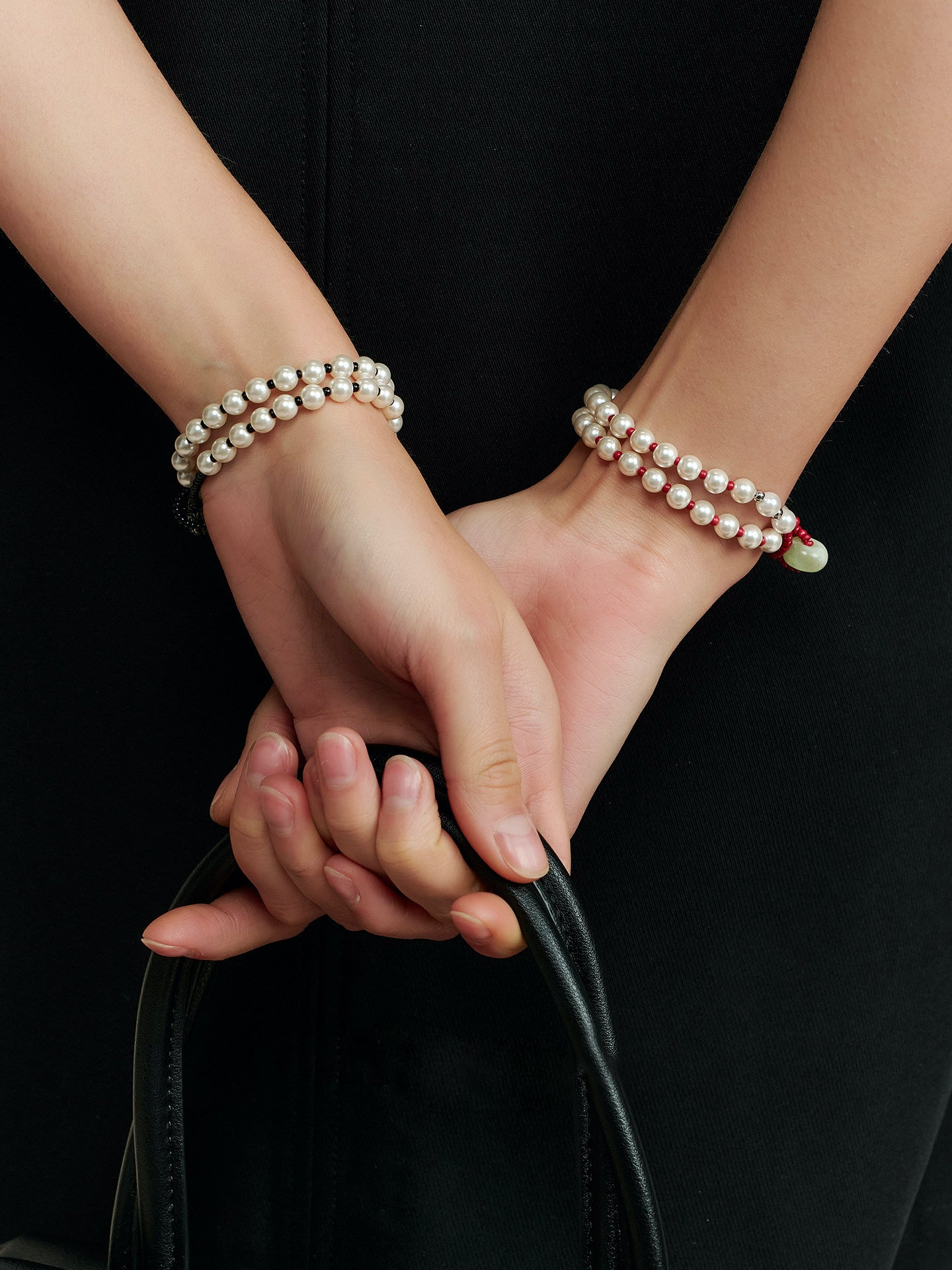 Model holding a black bag while wearing the Fairyokai Lunar Chord double-layer faux pearl bracelet on both wrists.
