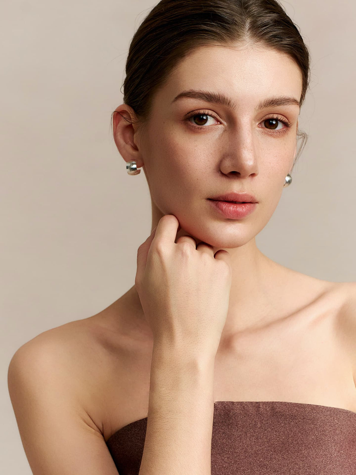 Model in a strapless top wearing Fairyokai Moon Trace sand-textured C-shape hoop earrings, resting her chin on her right hand, facing the camera on a neutral background.