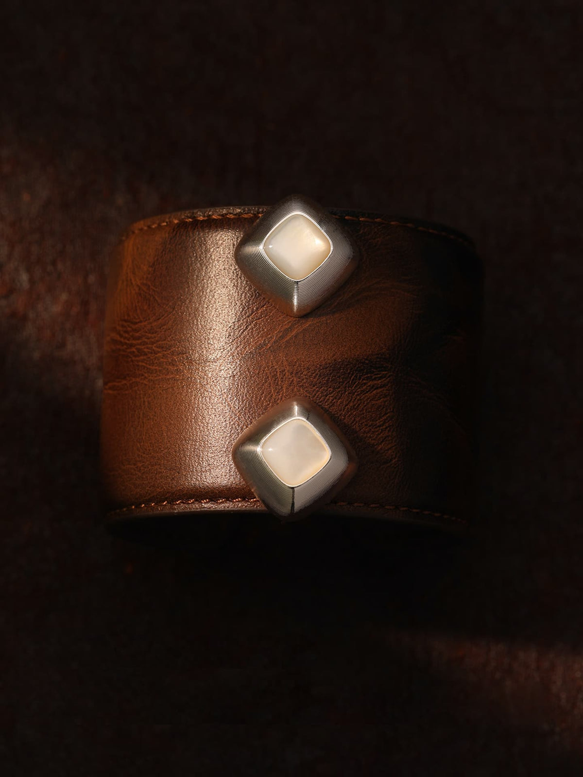 Pair of Fairyokai Mother-of-Pearl iridescent stud earrings flat-laid on a leather display object against a dark brown background, top-down view.