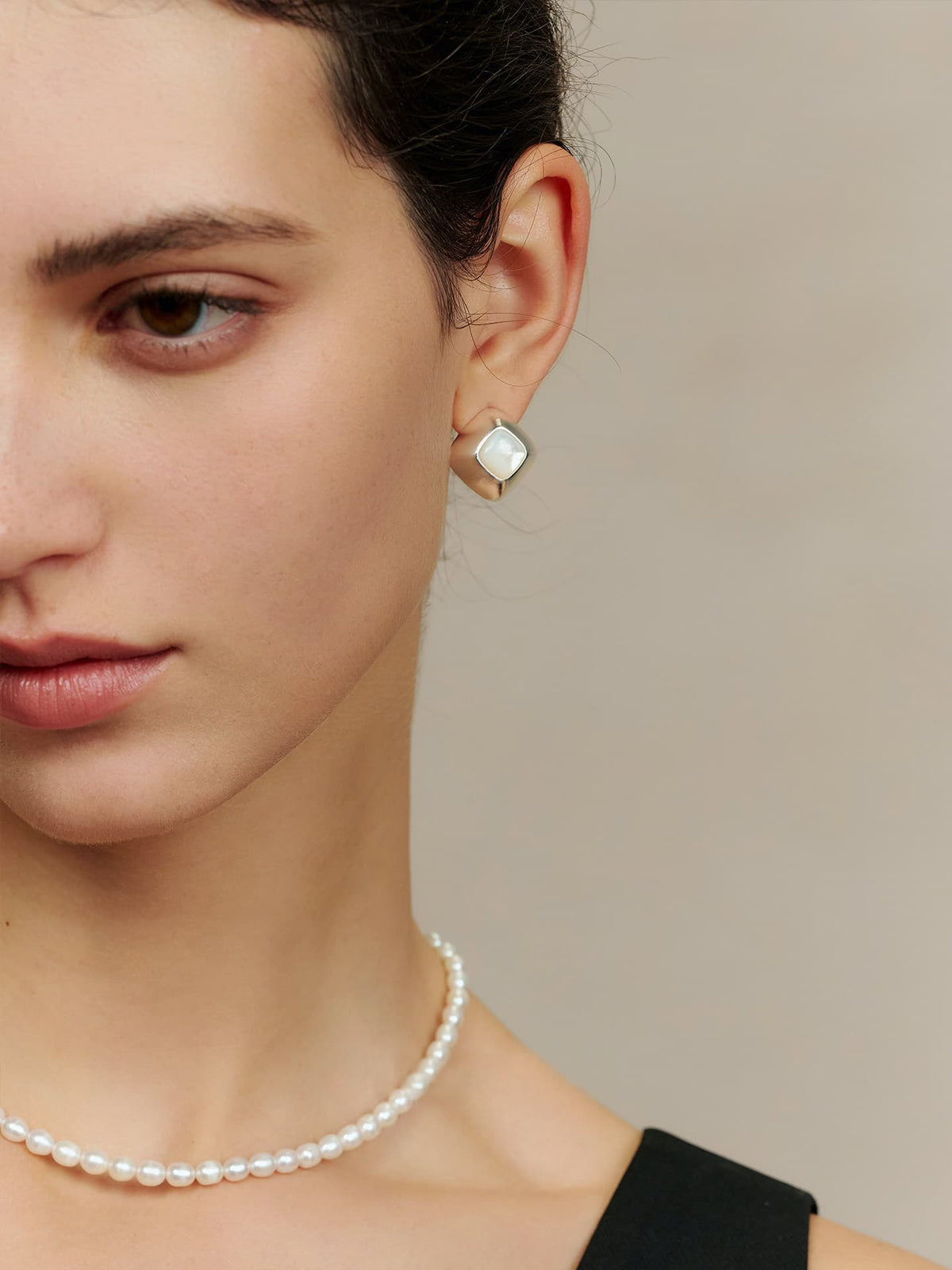 Close-up of a woman wearing a pearl necklace and Fairyokai Mother of Pearl Iridescent Stud Earrings, side view, against a neutral background