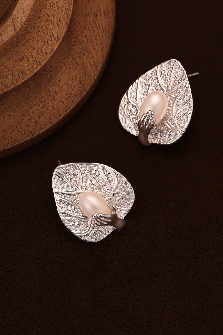 Fairyokai pair of silver leaf-shaped earrings with pearls on a dark surface with a wooden background