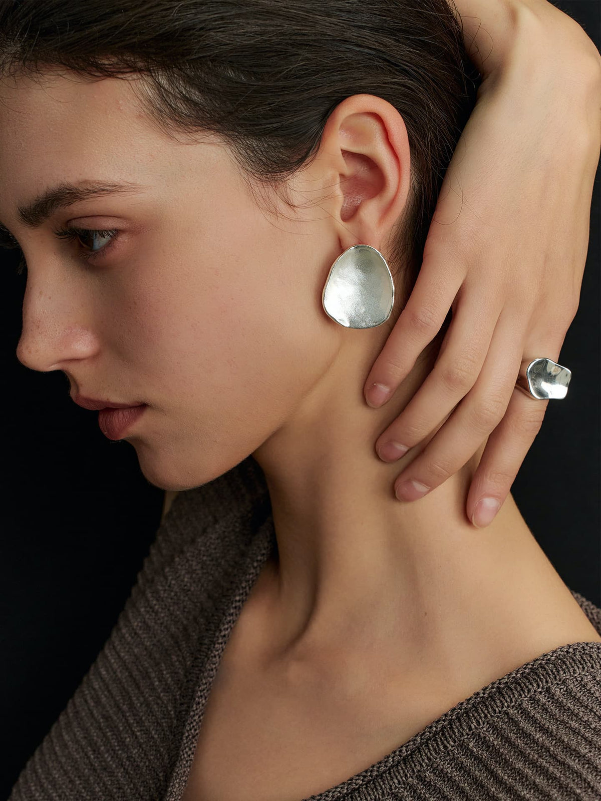 Close-up of a model in a solid sleeveless top, right hand resting on the left side of her neck, focusing on her left ear wearing Fairyokai Pillow Stone matte slice earrings, side profile against a black background.