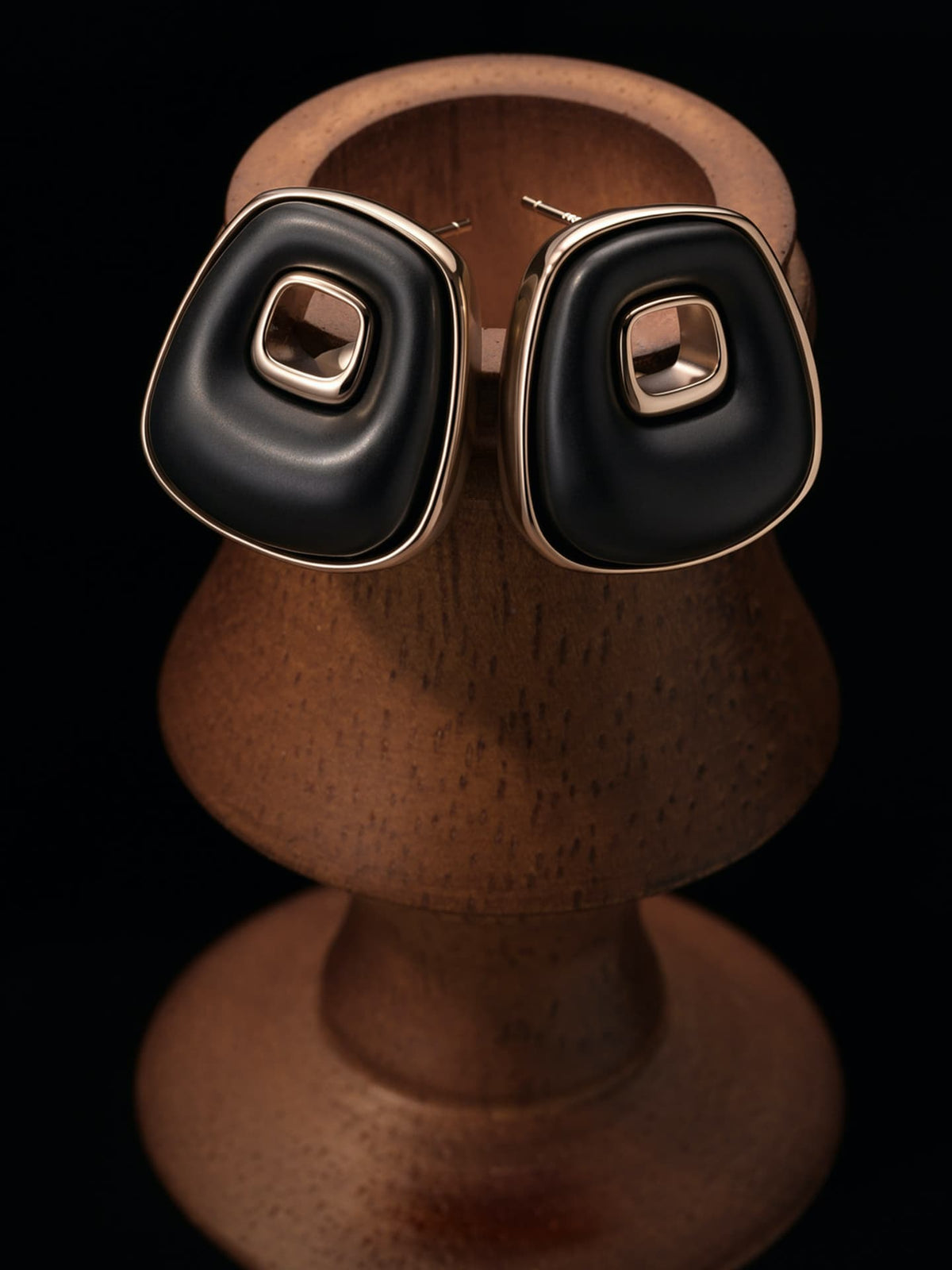 Fairyokai Resting Corner trapezoid ebony earrings hanging on a wooden display stand against a black background.