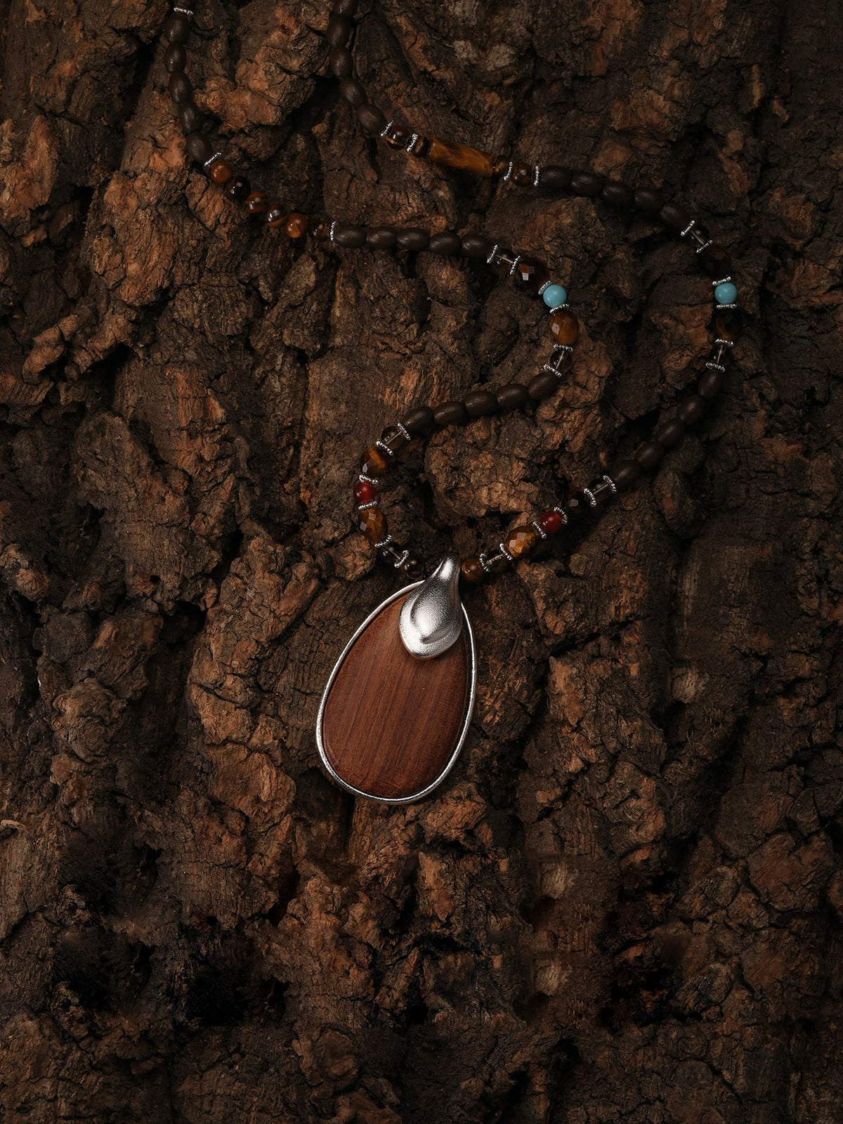 Fairyokai Return to Nature wood pendant necklace curved and laid flat on a dark brown wood grain background, top-down view.