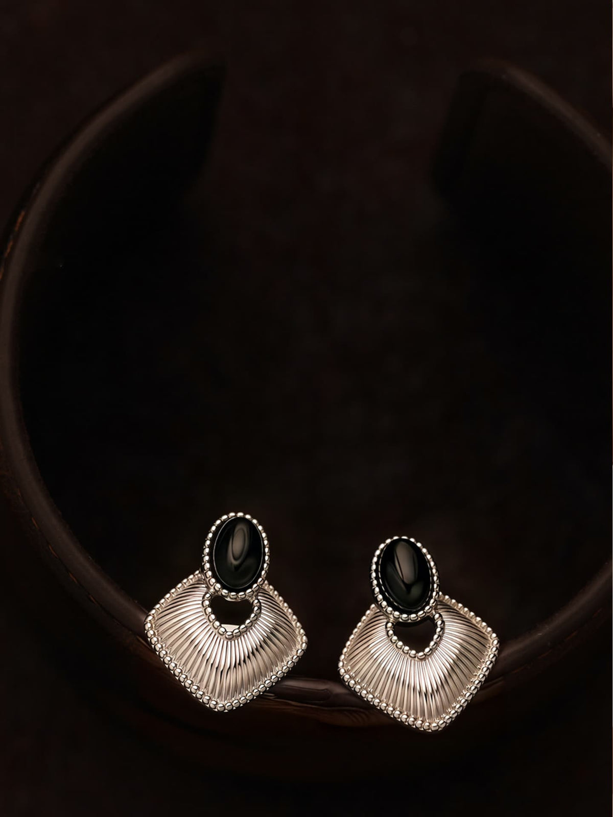 Fairyokai Silent Order black agate earrings flat-laid on a dark brown background, top-down detail view.