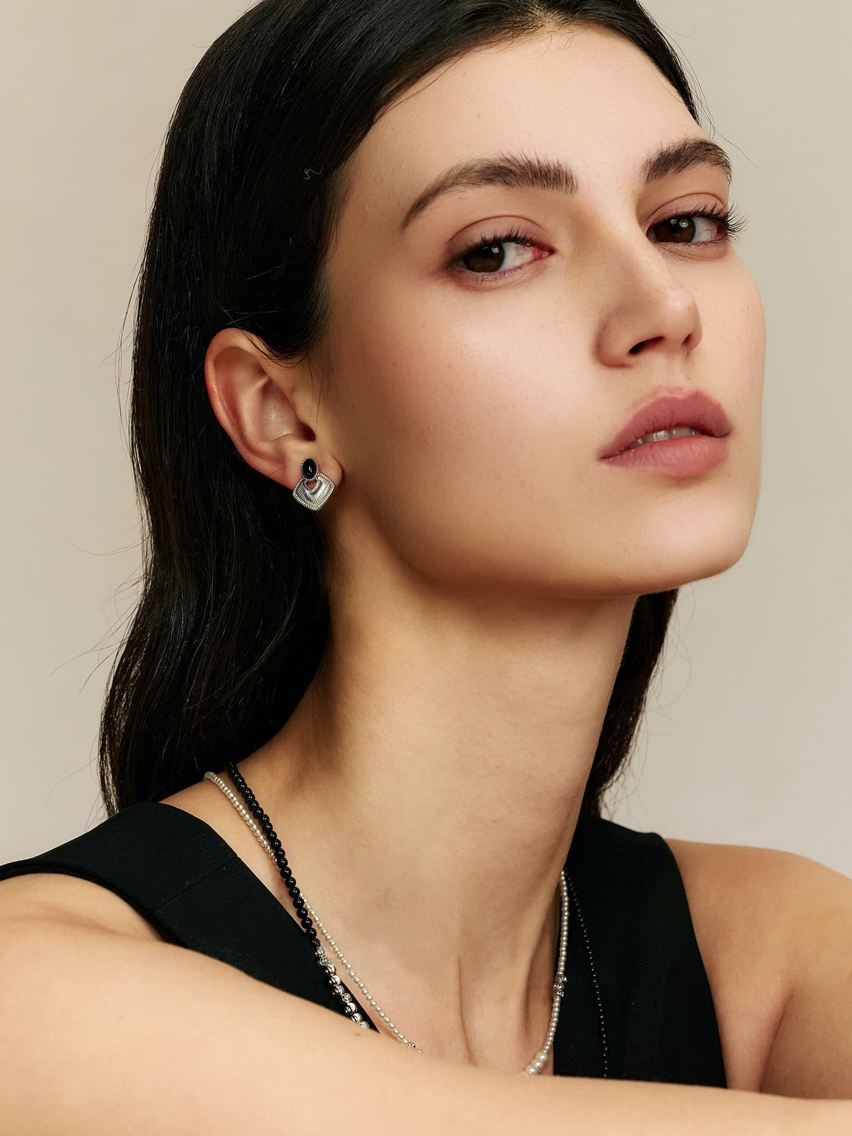 Side profile of a model with dark hair, head slightly lifted, looking at the camera, wearing Fairyokai Silent Order black agate earrings, a deep V-neck black dress, and a silver necklace.