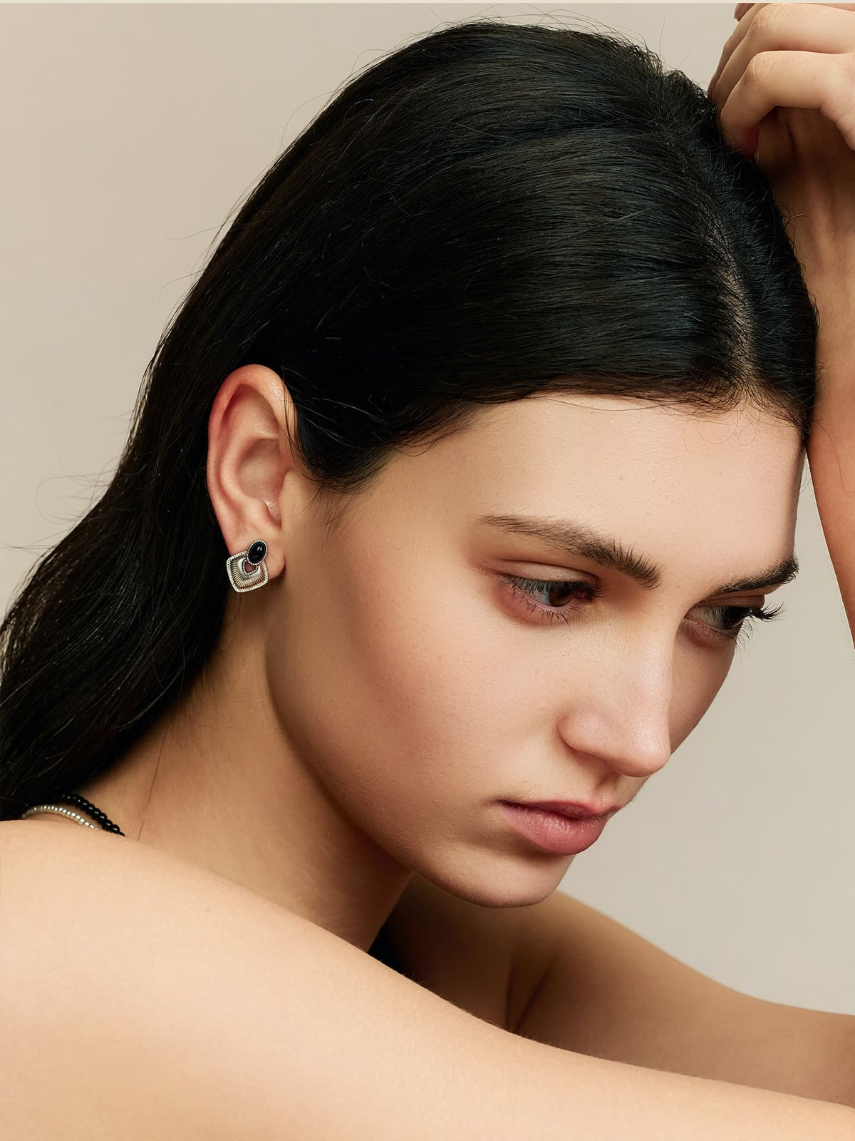 Side profile of a model with dark hair, resting her head on her hand, wearing Fairyokai Silent Order black agate earrings, looking down to the left, against a neutral background