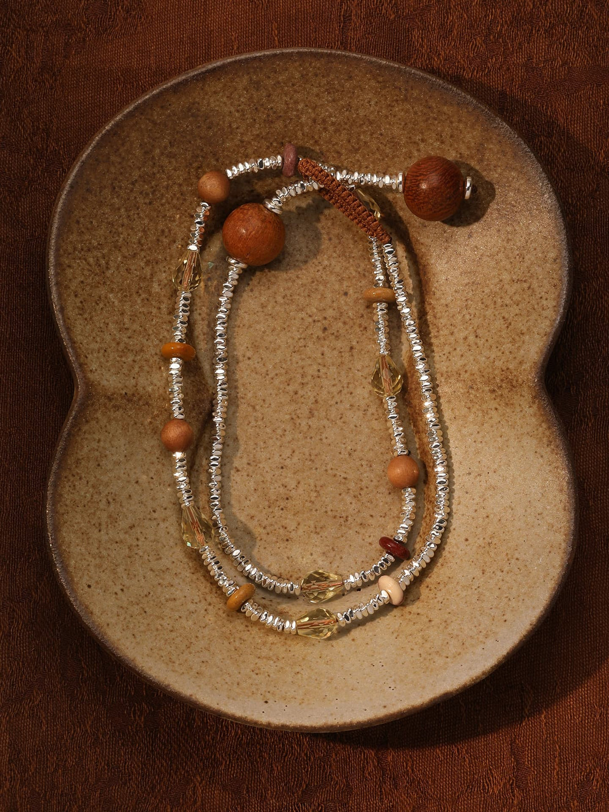 Fairyokai Soft Pure Light mixed stone braided bracelet flat-laid on a sculptural ceramic plate, showing pale stones and warm wood-like beads.