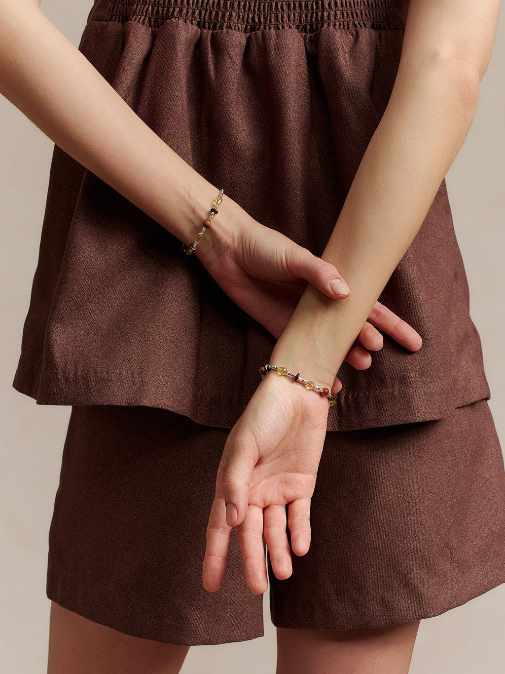 Model standing in a brown outfit wearing the Fairyokai Soft Pure Light mixed stone braided bracelet on both wrists, back to the camera.