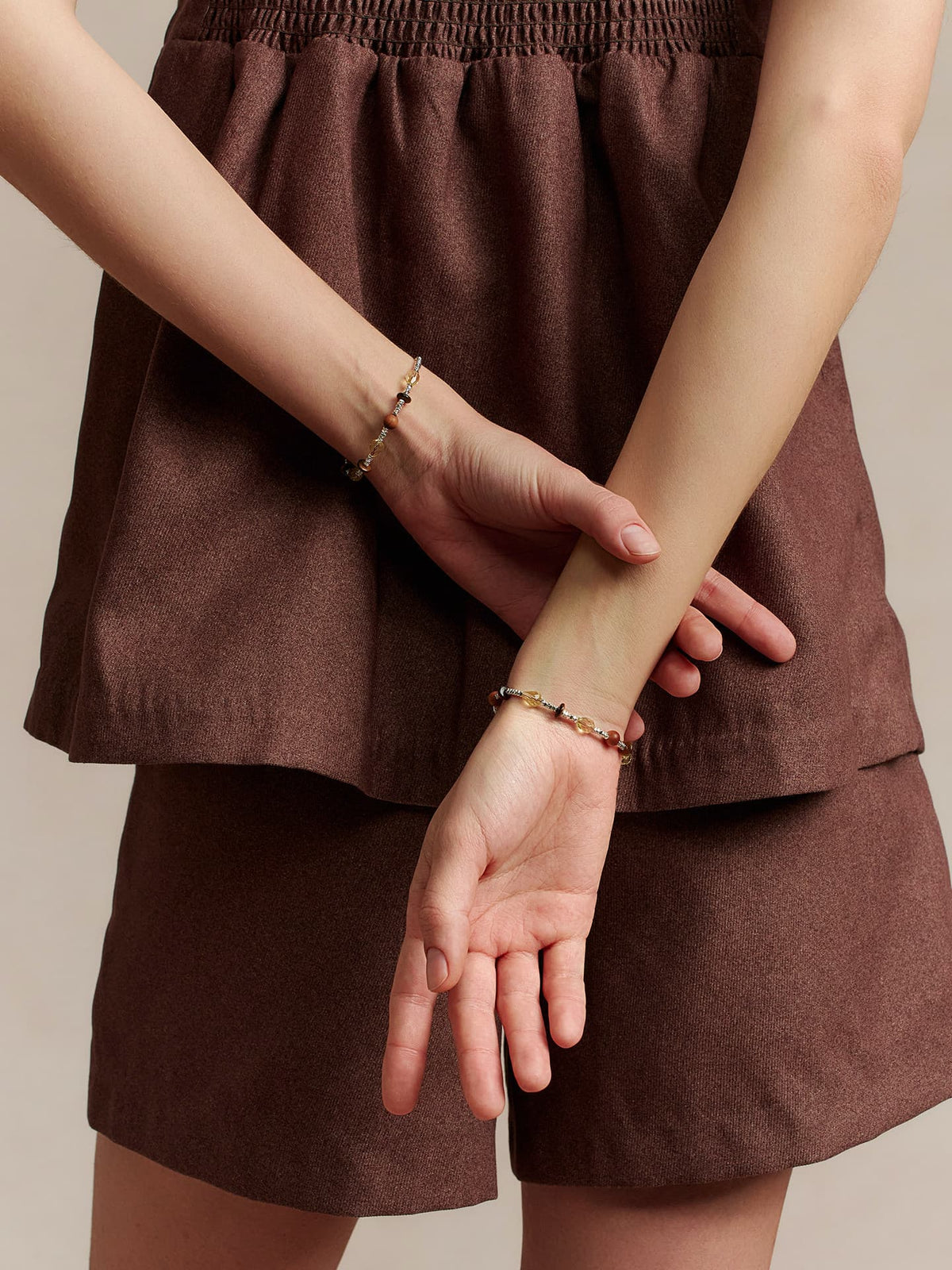Model standing in a brown outfit wearing the Fairyokai Soft Pure Light mixed stone braided bracelet on both wrists, back to the camera.
